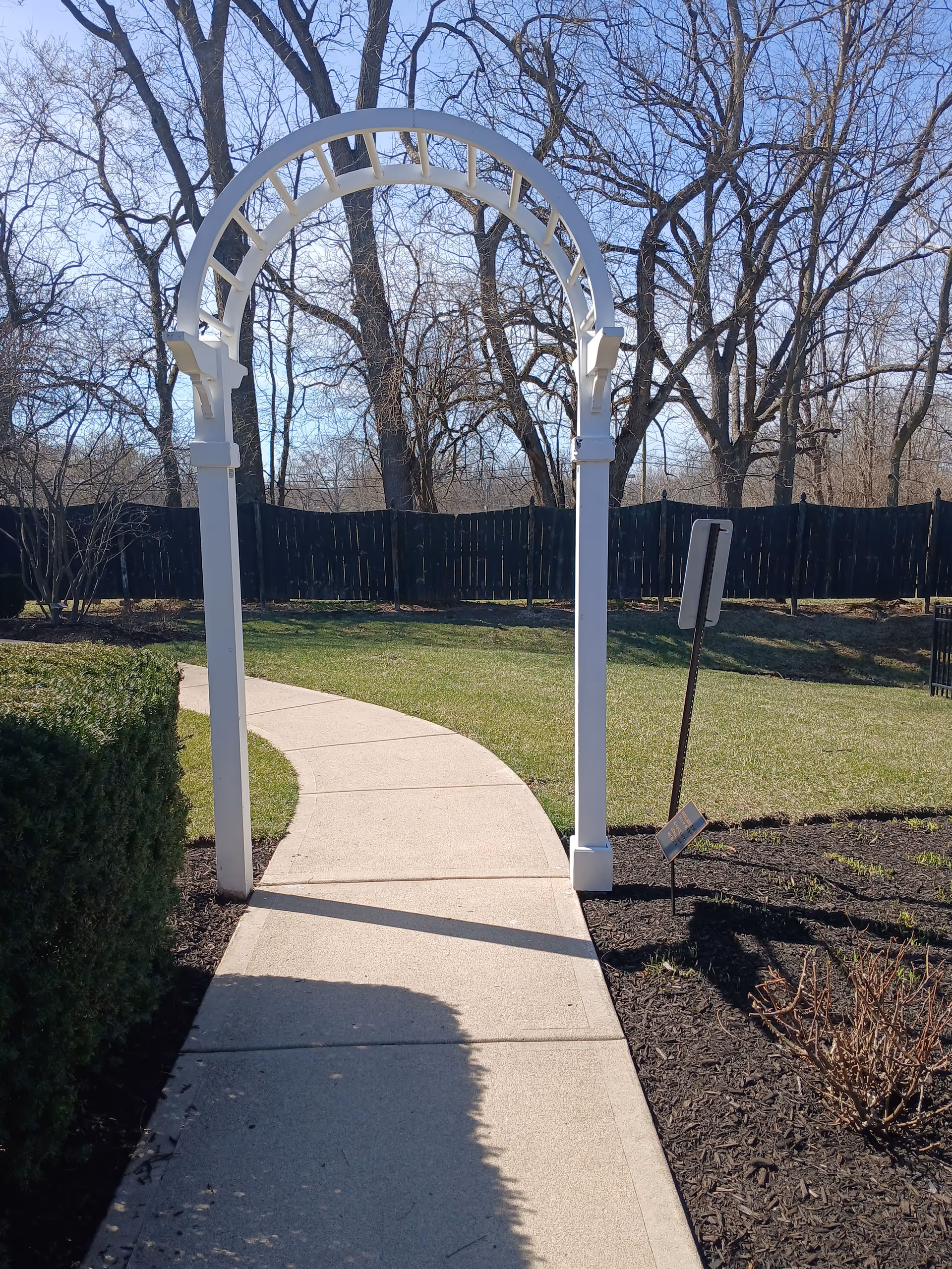 White arched pergola over a curved concrete walkway in a fenced outdoor space