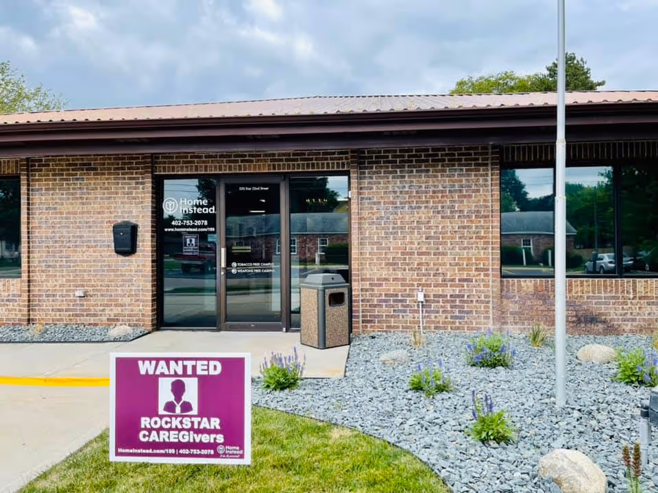 Brick building entrance with glass doors and a purple sign reading 'Wanted Rockstar Caregivers' outside.