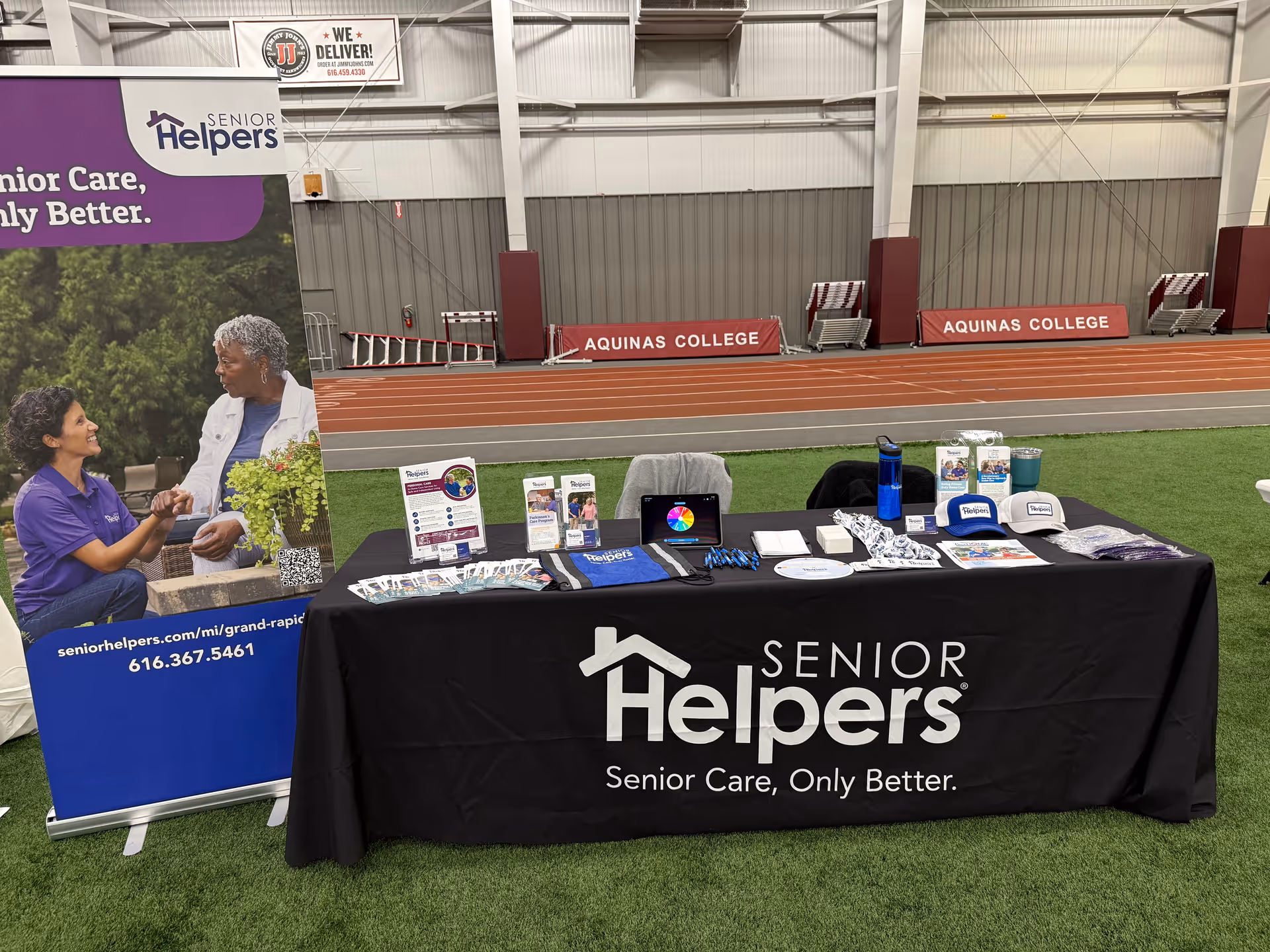 Promotional Senior Helpers booth with banner and table inside an indoor athletic facility.