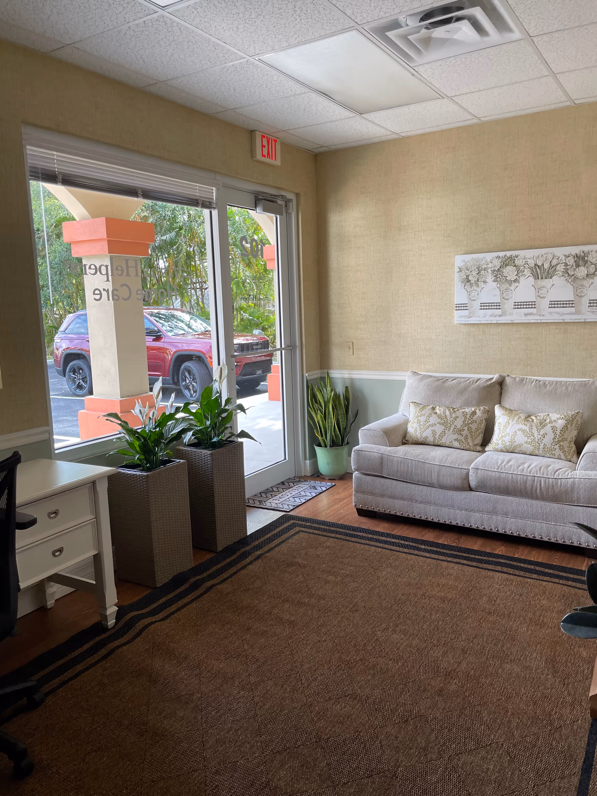 Cozy interior lobby with beige sofa, plants, desk, and glass entrance doors.