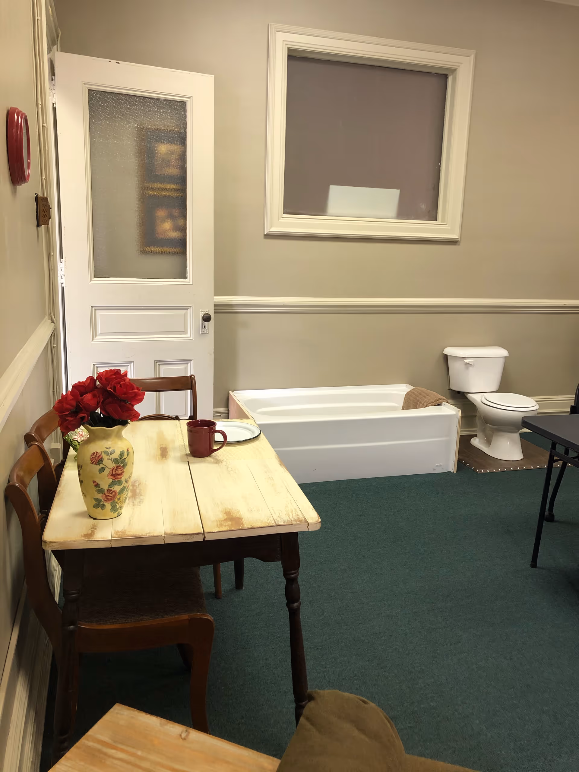 A small wooden table with chairs beside a bathtub and toilet in a beige room.