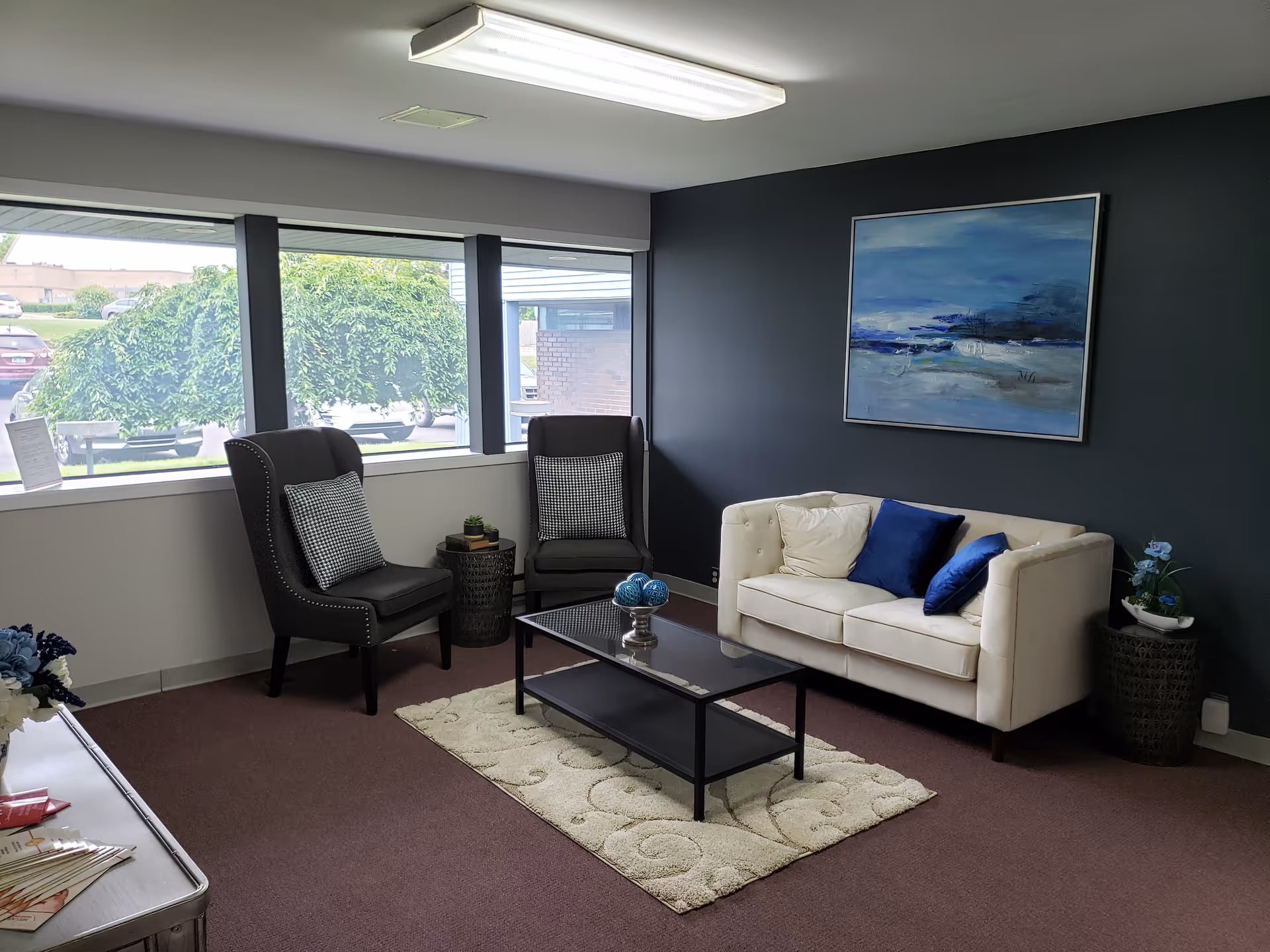 A modern waiting lounge with two chairs, a sofa, coffee table, rug, and wall art.