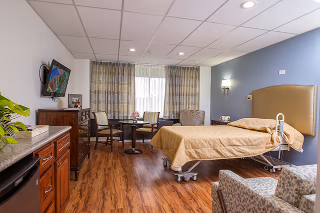 A hospice patient room with a single bed, sofa, chairs, TV, and wood-floored interior.