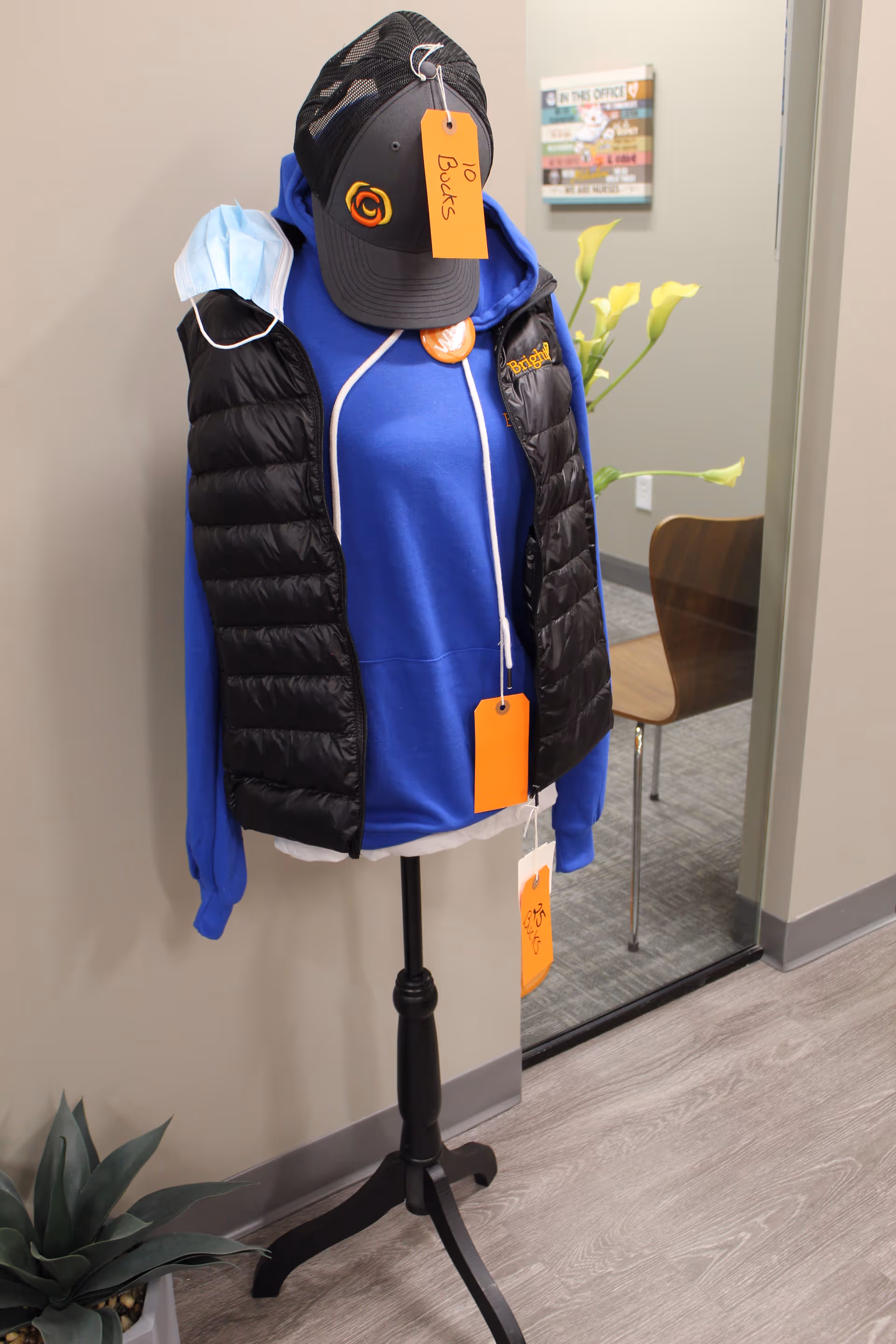Mannequin displays blue hoodie and black puffer vest with orange tags indoors.