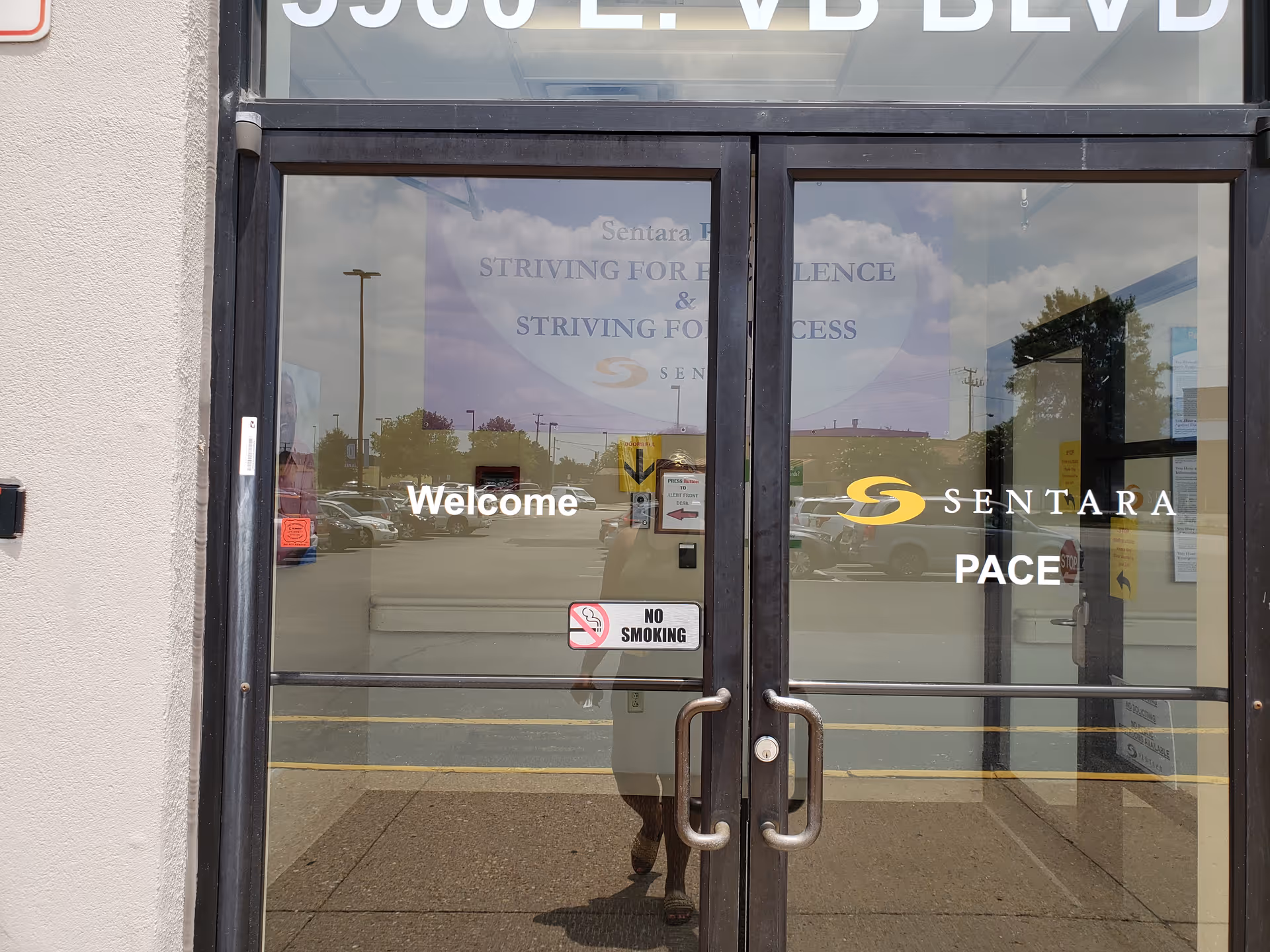 Glass double doors showing Sentara PACE welcome signage with reflections of cars outside.