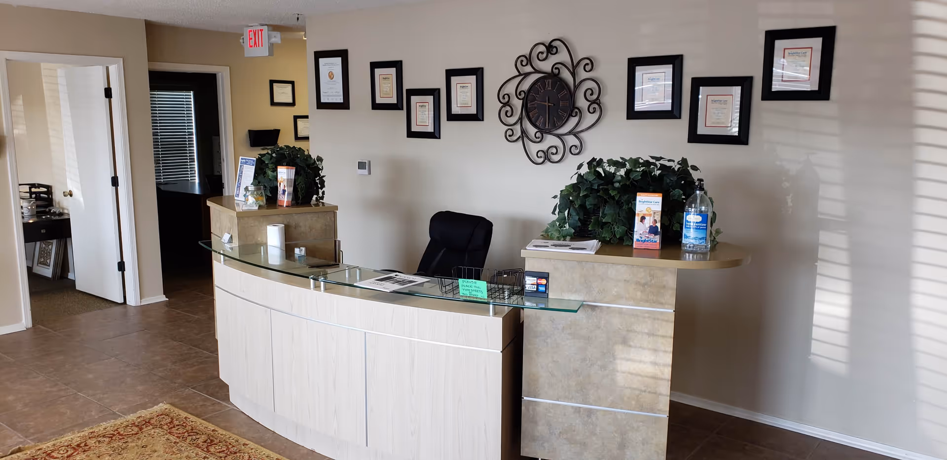 Reception desk with glass top, framed certificates, and plants in a BrightStar Care facility lobby.