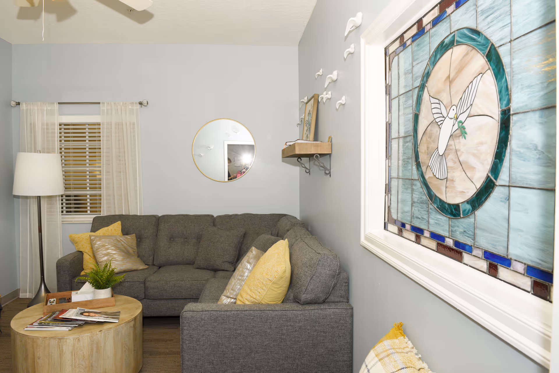 A cozy living room with gray sectional sofa, round coffee table, and stained glass window.