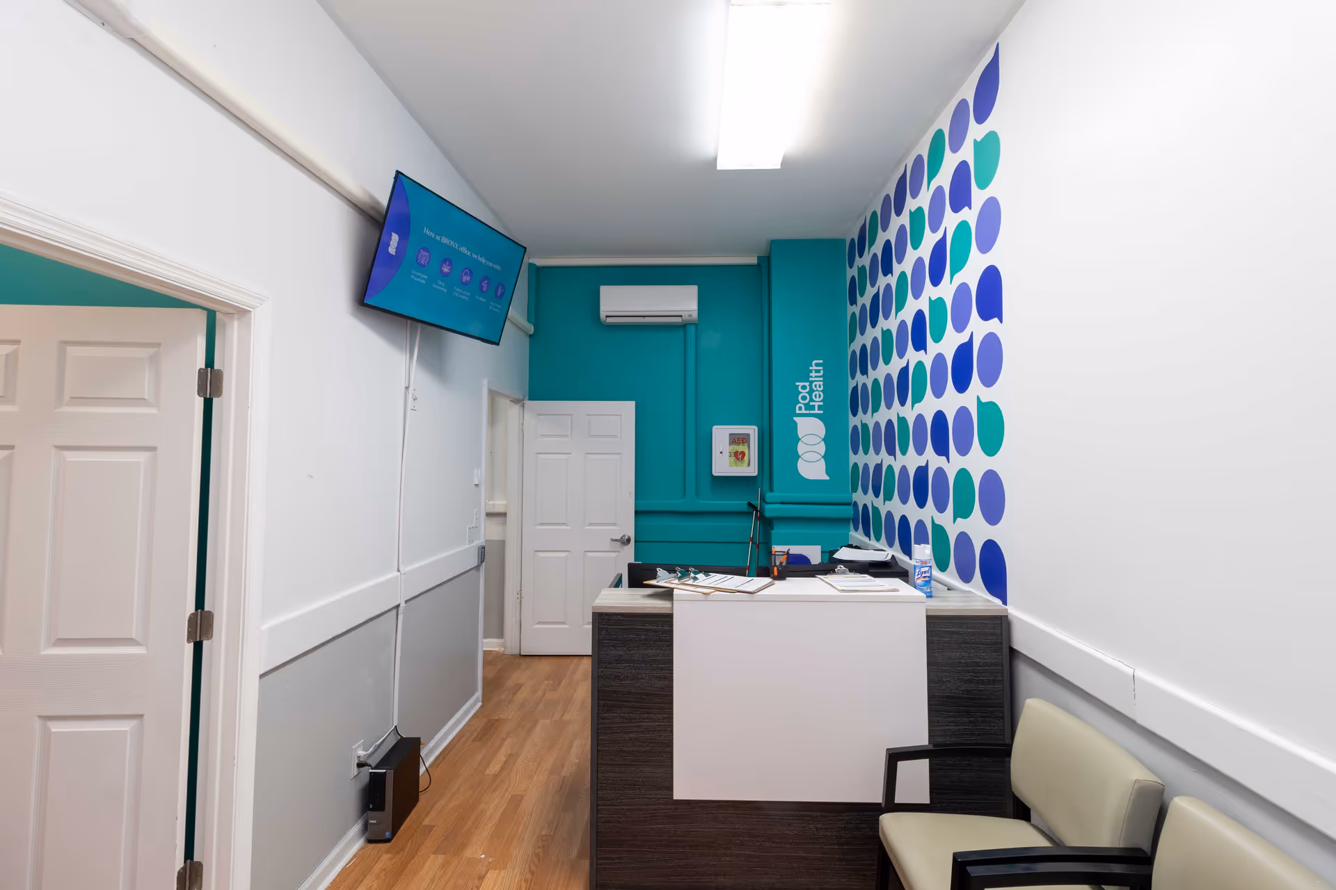 Modern reception area with teal accent wall, wall art, and a front desk at Pod Health.