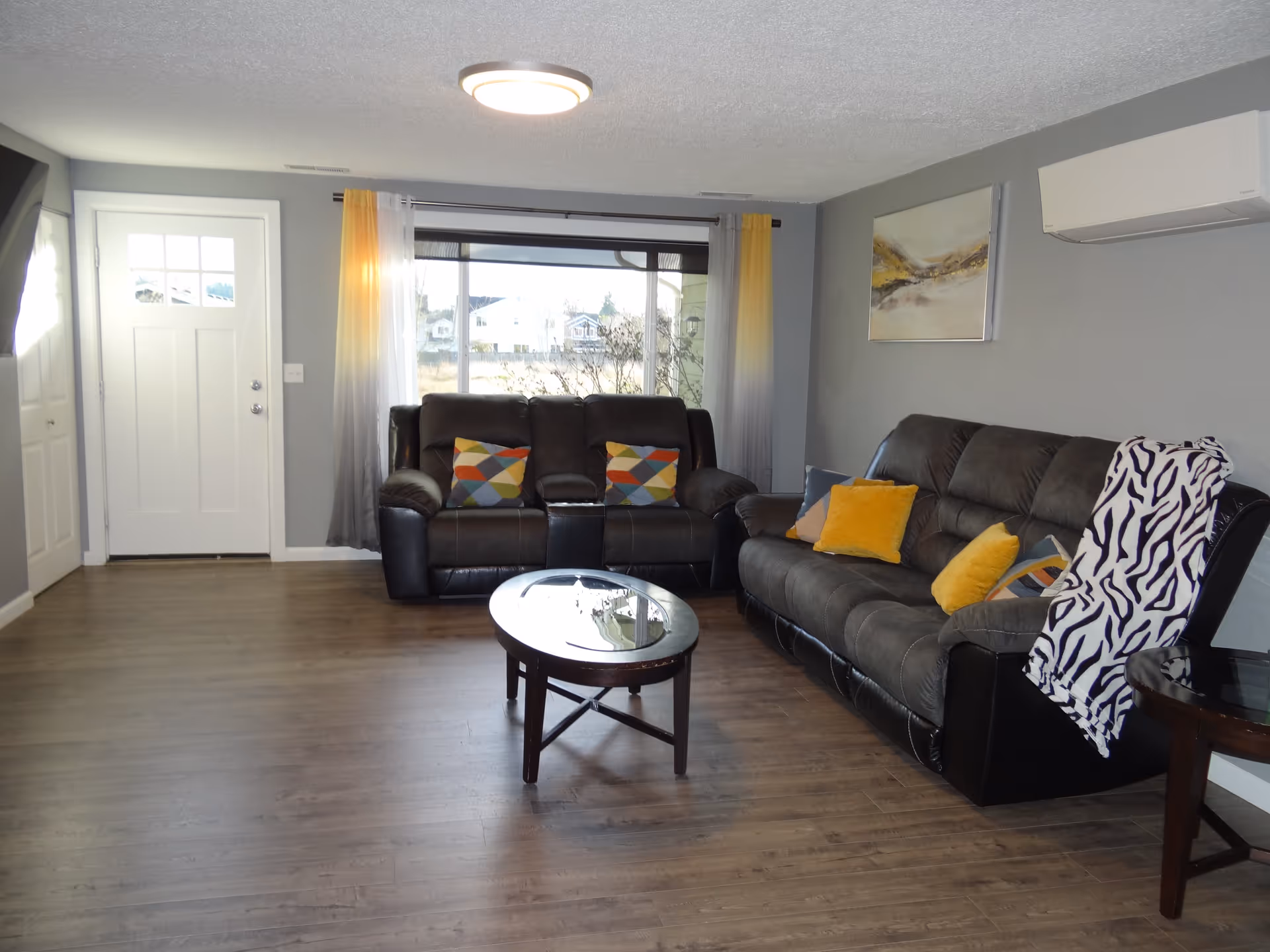 A contemporary living room with two black leather sofas, a round coffee table, and large window.