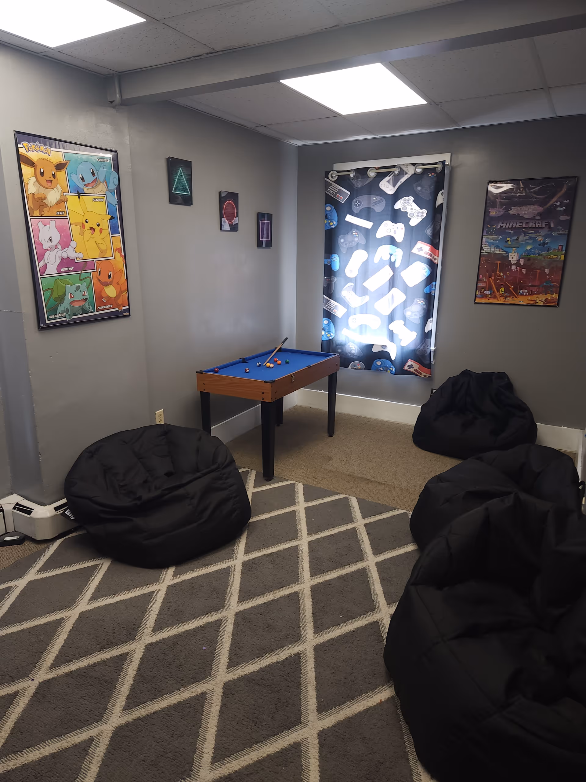 A small game room with a blue pool table, bean bag chairs, and wall posters.