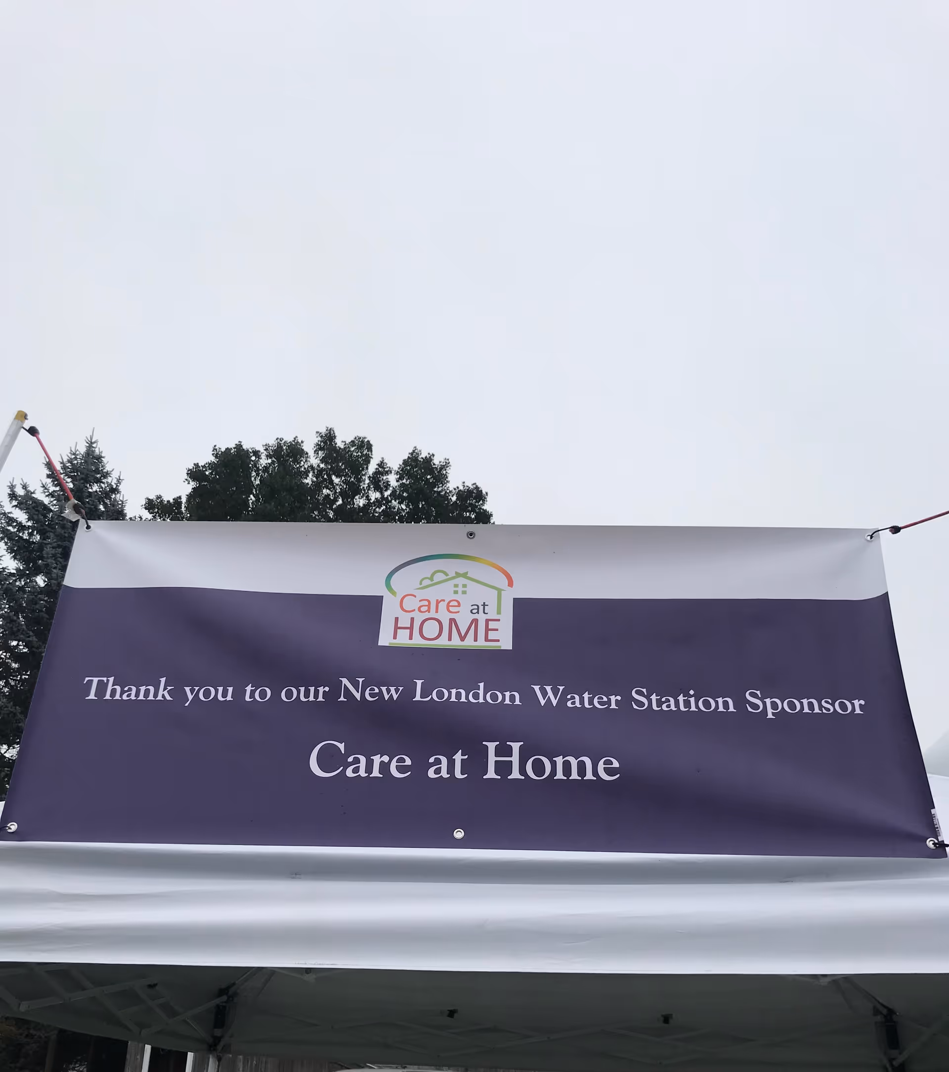 Large banner advertising Care at Home attached to a white tent outdoors.
