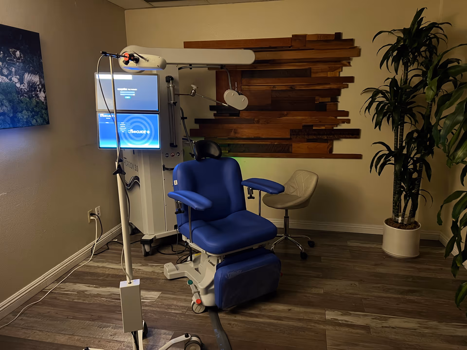 Blue reclining medical chair with screens and equipment in a clinic room.