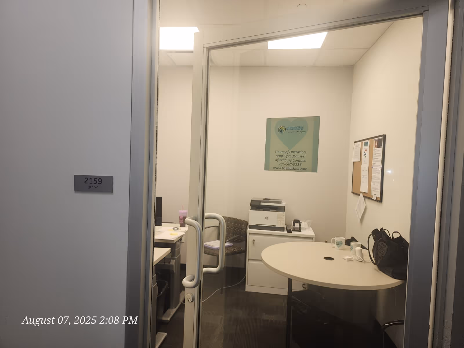 Office-like reception area with glass door, round table, printer, and bulletin board.