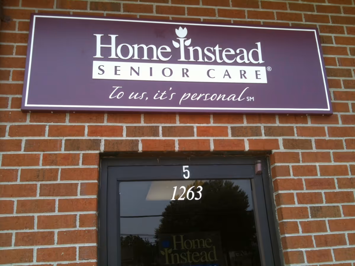 Purple Home Instead Senior Care sign above a glass door on a brick building.
