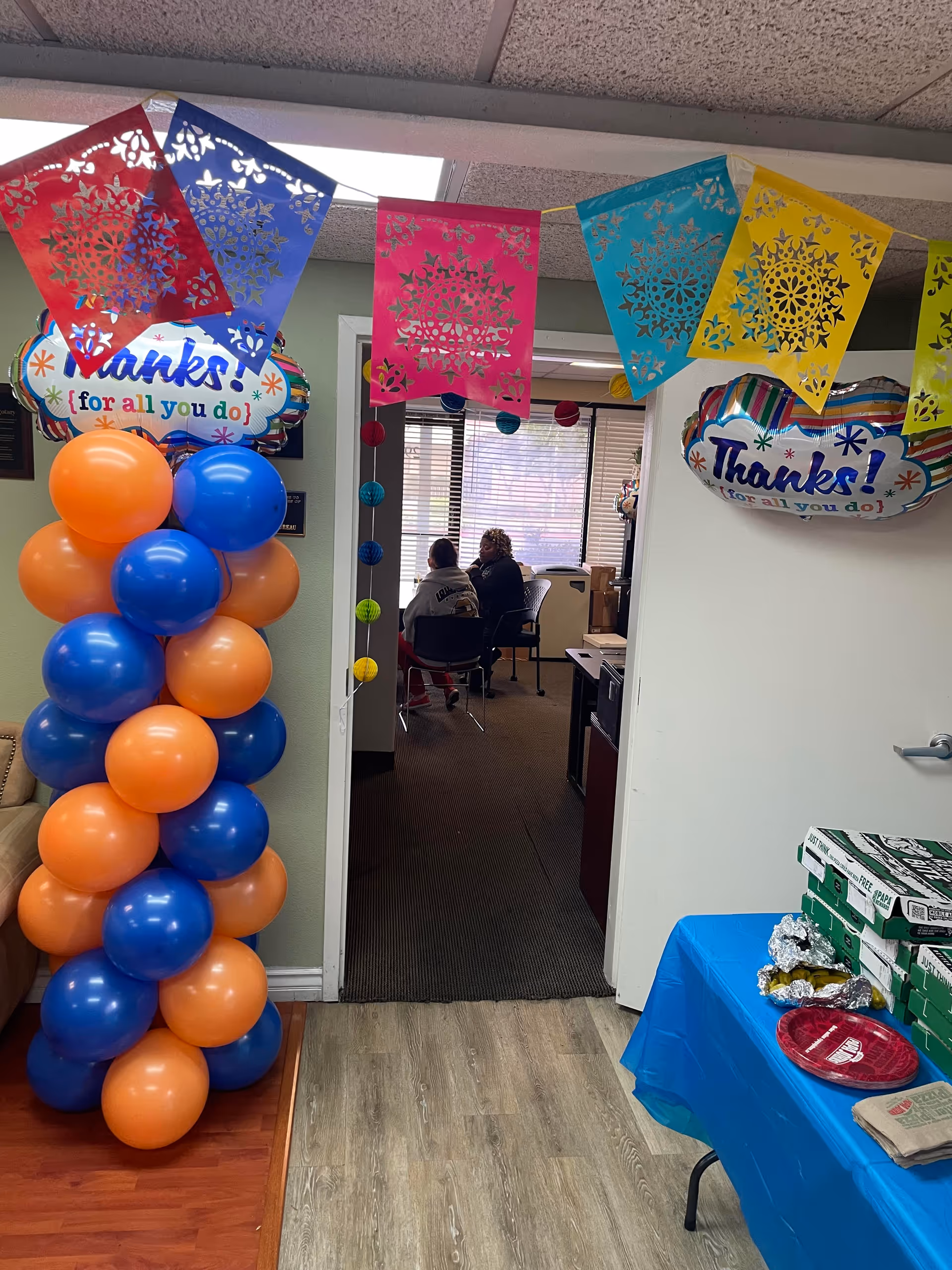 Festive indoor scene with colorful banners, balloons, and people seated in a back room.