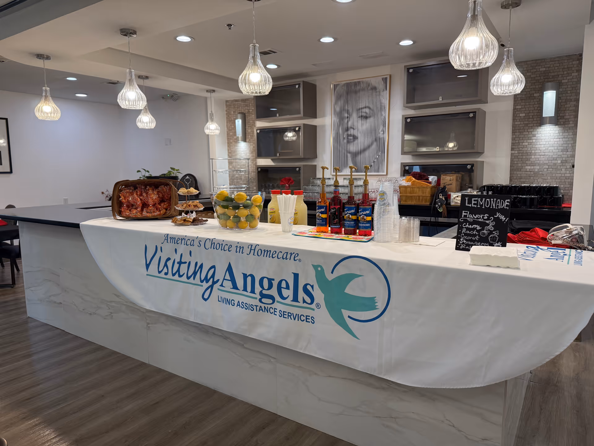 Interior with a curved service counter displaying food and beverages under Visiting Angels banner.