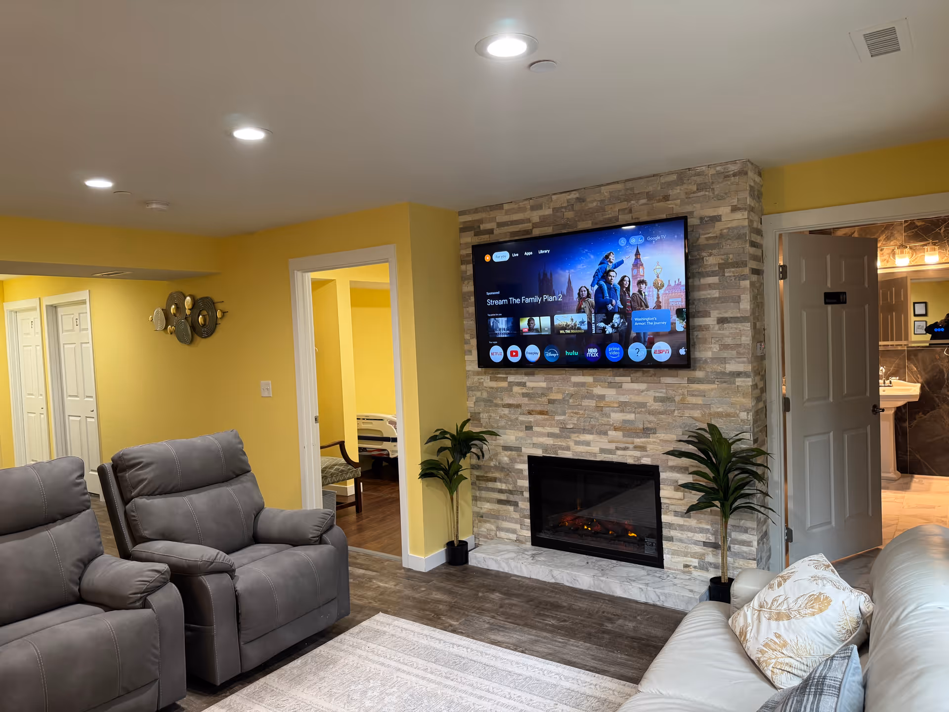 Cozy living area with yellow walls, stone fireplace, wall-mounted TV, and reclining chairs.
