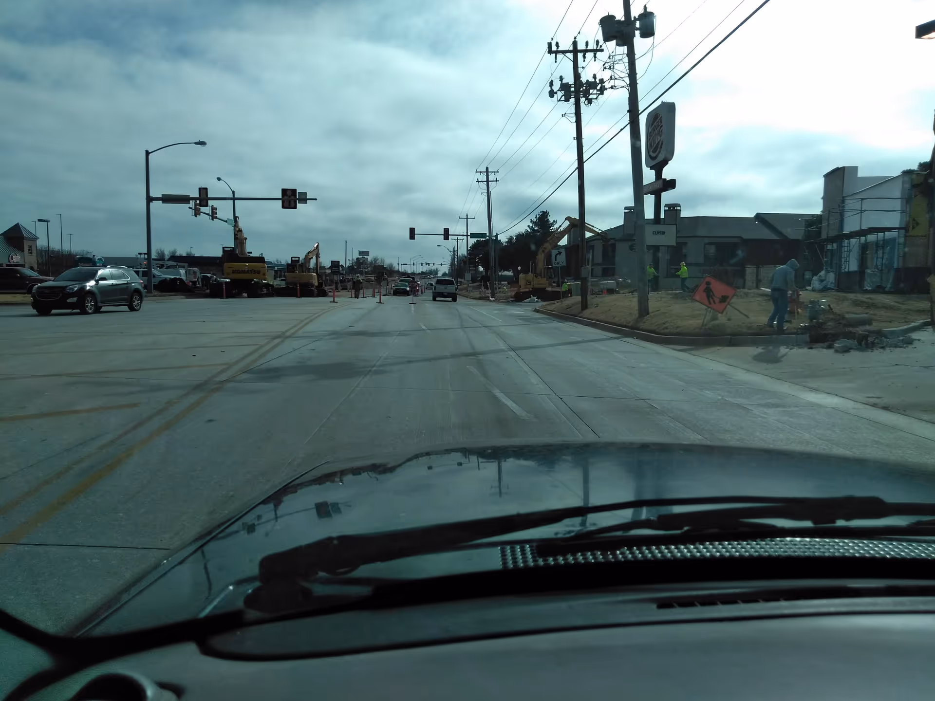 View from inside a car on a road under construction with excavators and workers.