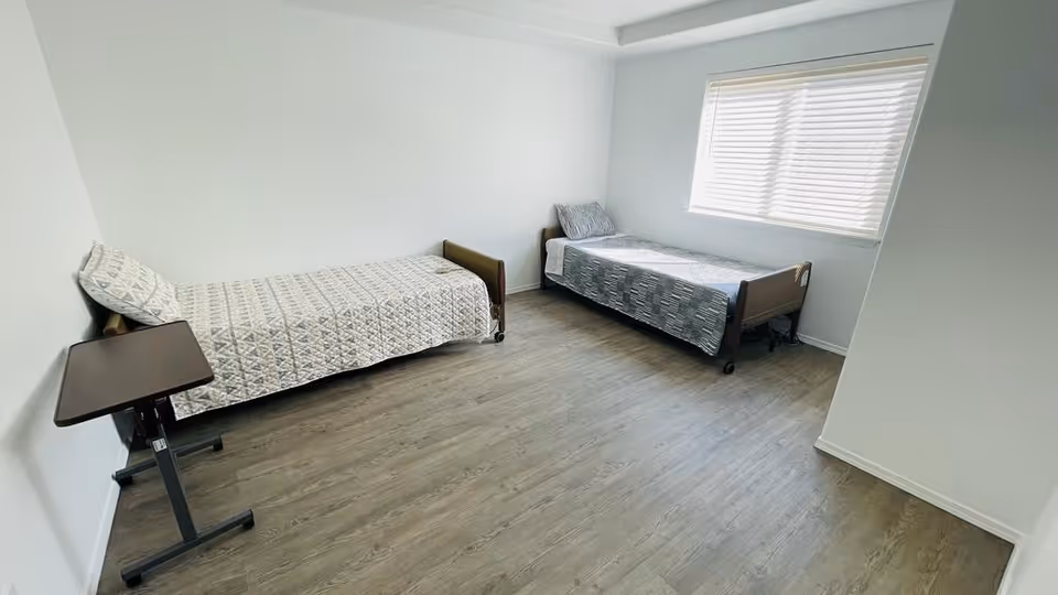 A clean, empty shared bedroom with two single beds and a window.