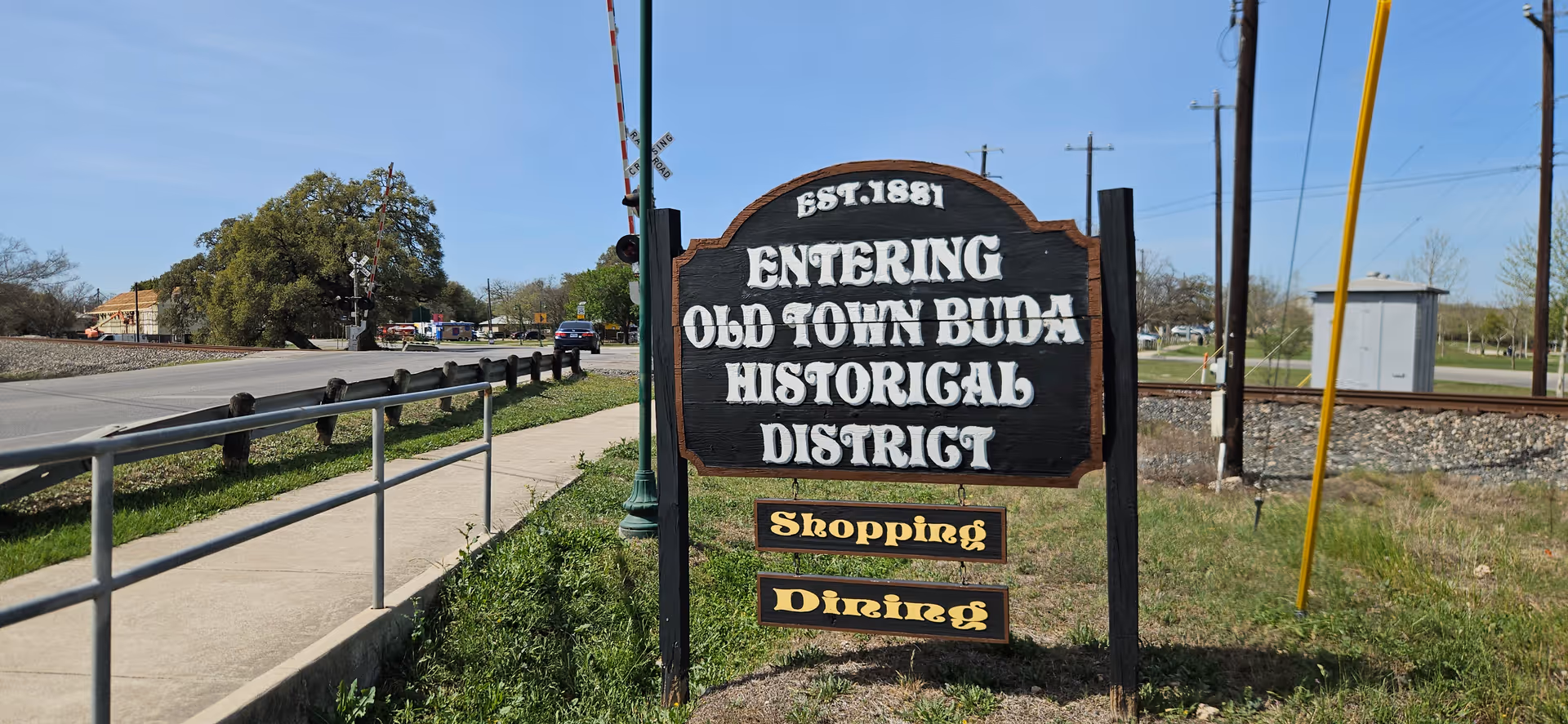 Outdoor wooden sign reads Entering Old Town Buda Historic District.