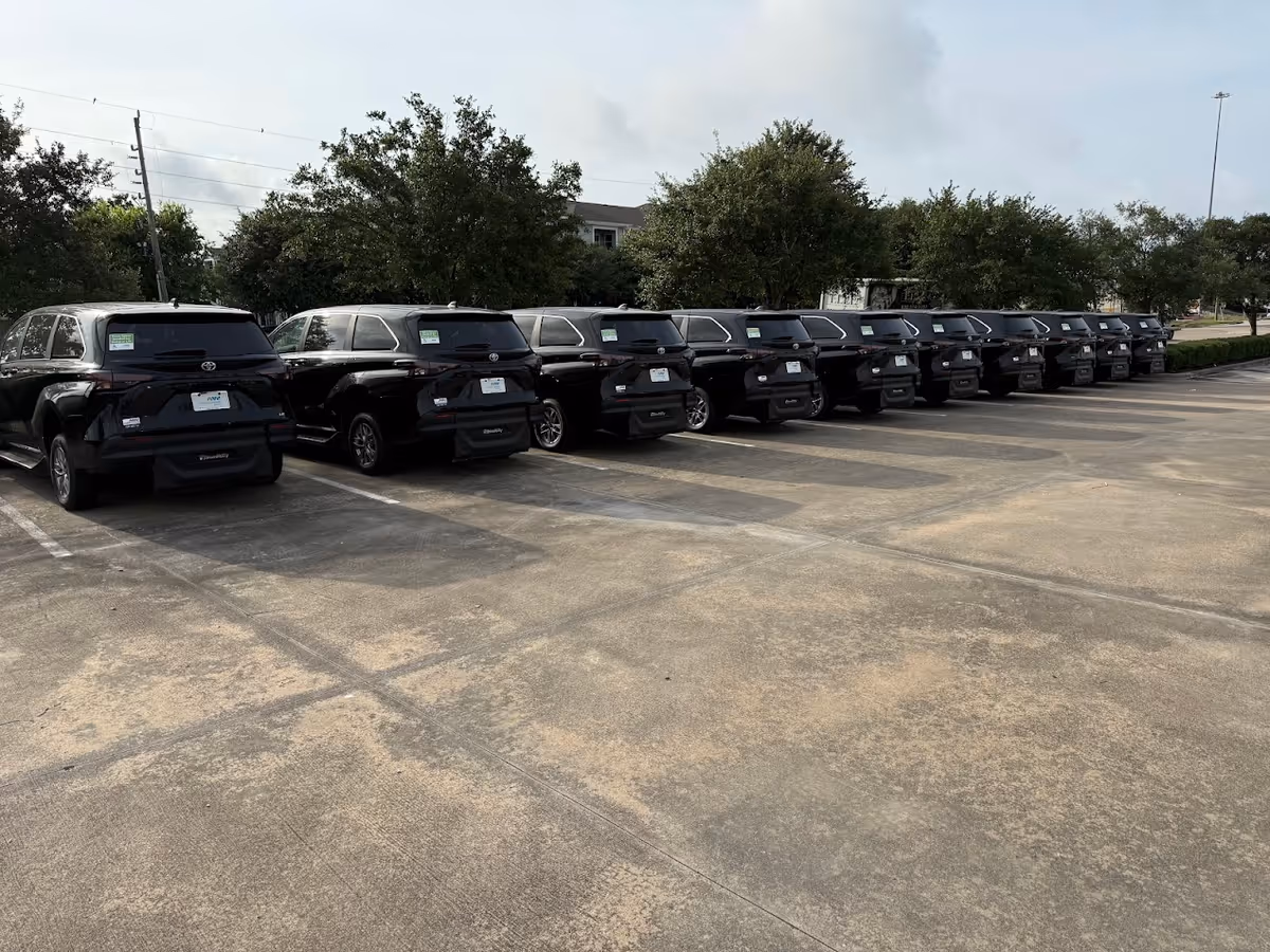 Row of black SUVs parked in a large outdoor lot with trees in the back