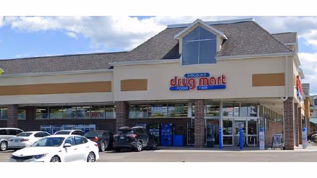 Exterior view of a Discount Drug Mart storefront with parked cars in front.