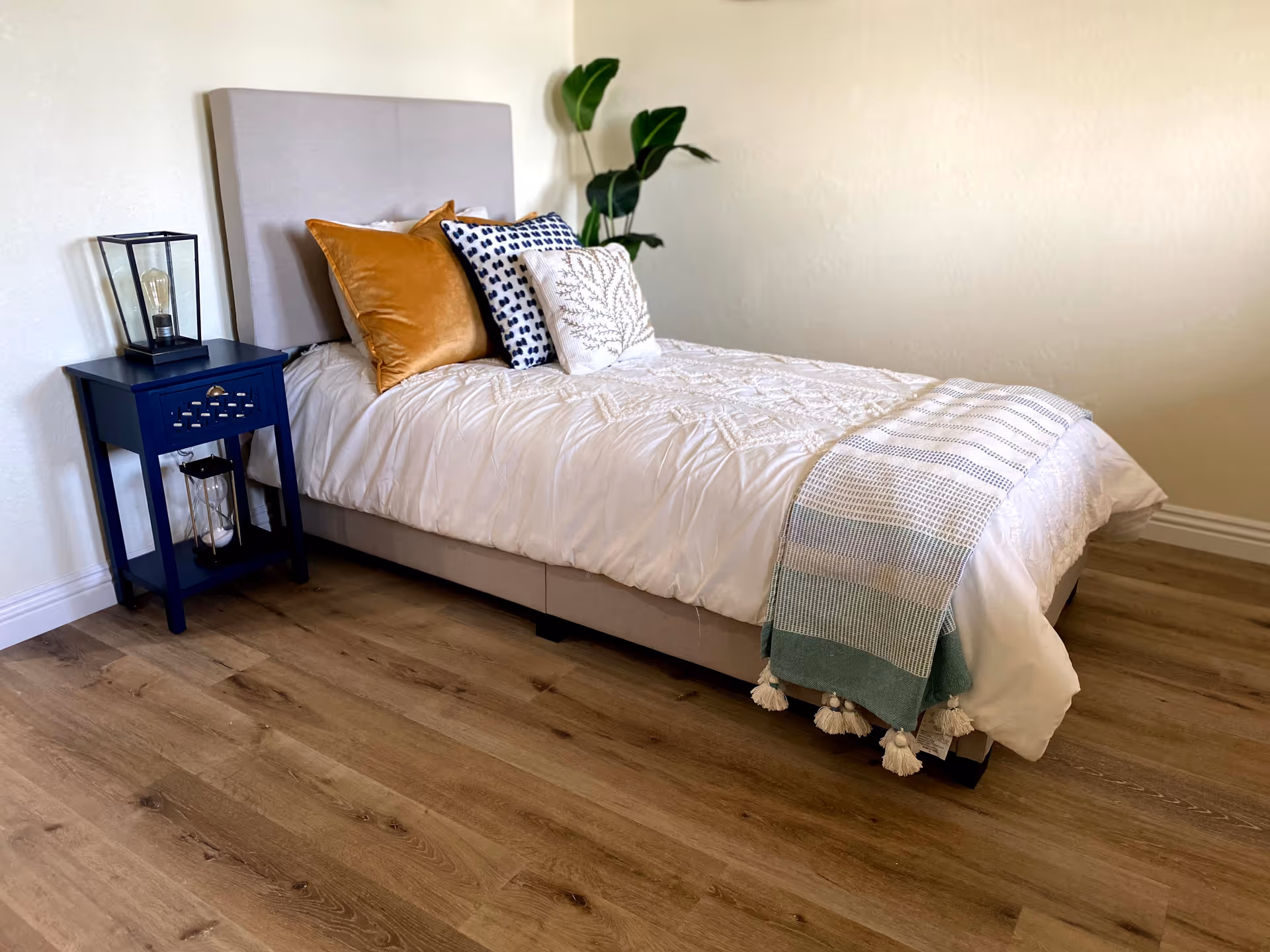 Cozy Mountain View Manor bedroom with a plush bed, blue nightstand, and leafy plant.