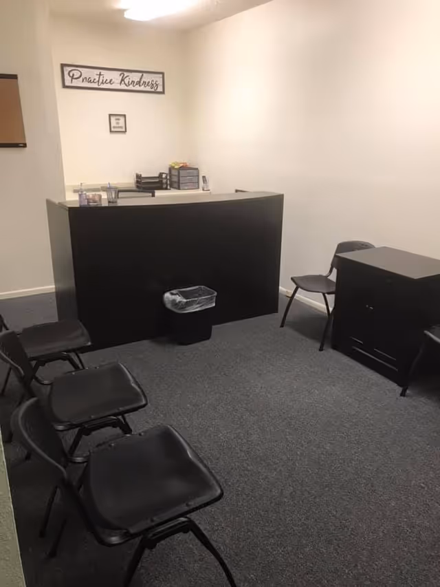Curved reception desk with black chairs in a small waiting area.