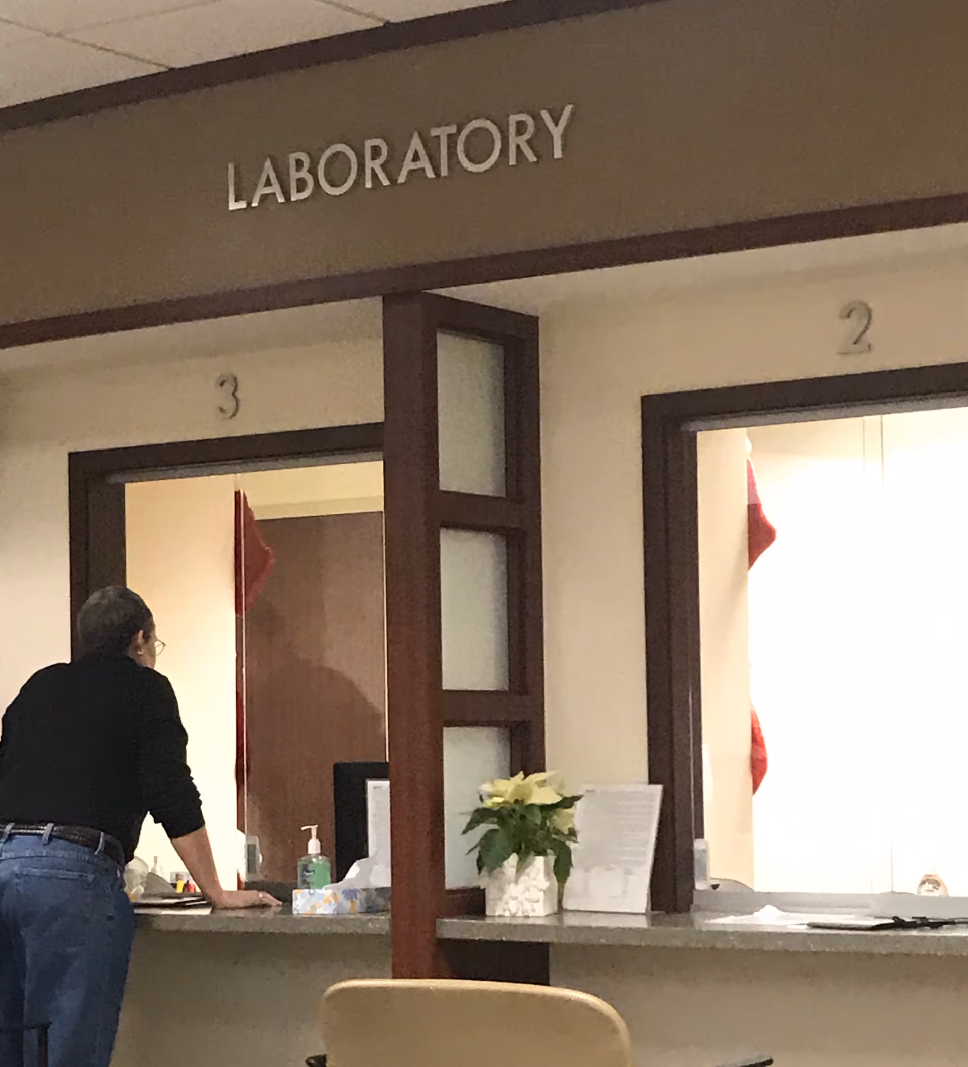 A person stands at a reception counter beneath a LABORATORY sign.