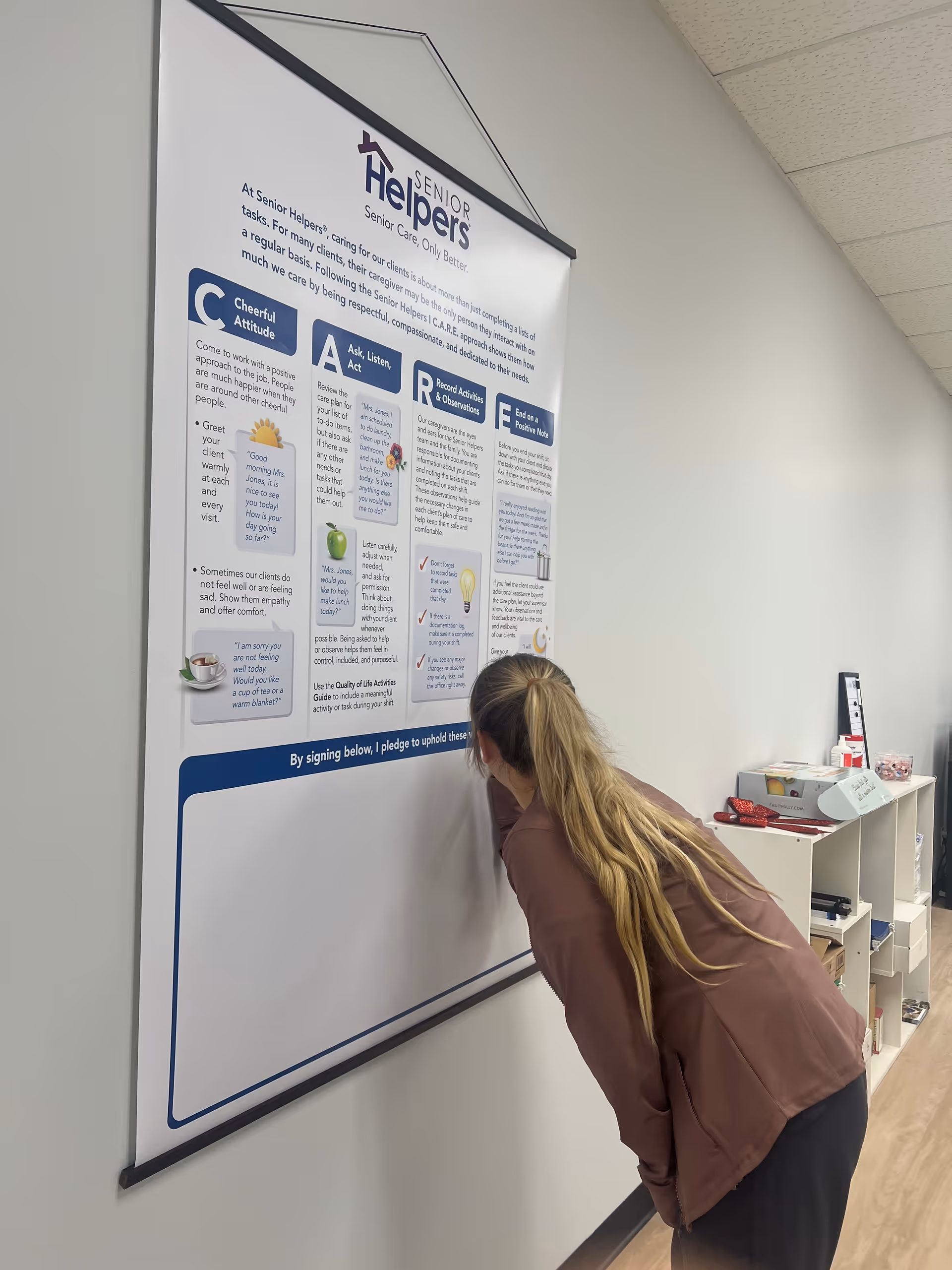A woman leans in to read a large Senior Helpers poster mounted on the wall.