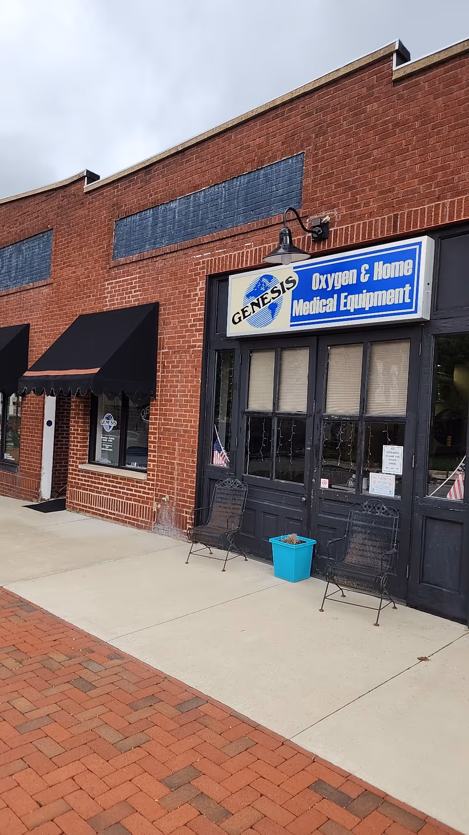 Brick storefront with Genesis Oxygen & Home Medical Equipment sign, black doors, chairs, and a planter.