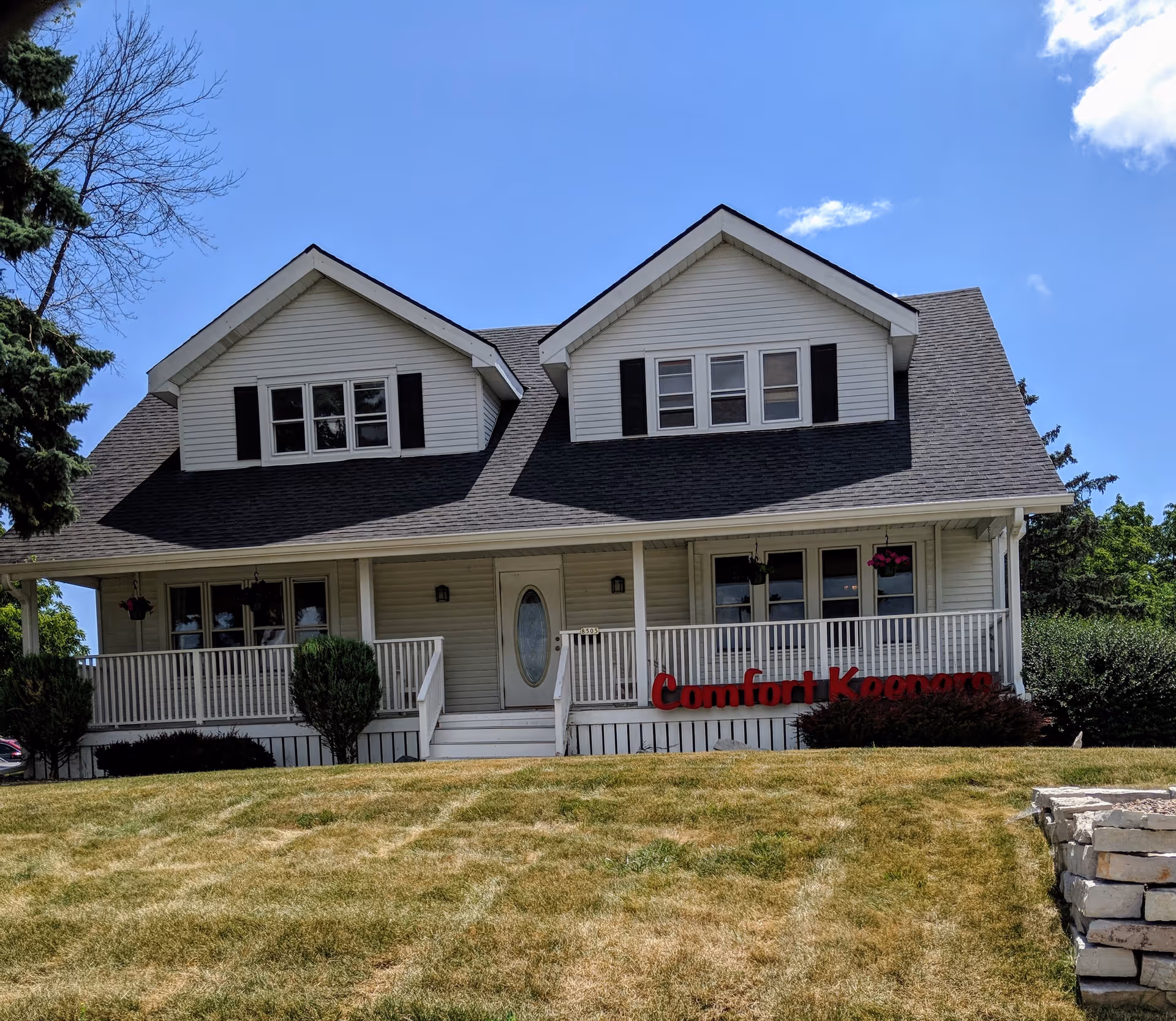Two-story house-style senior care building with a front porch and red Comfort Keepers sign.