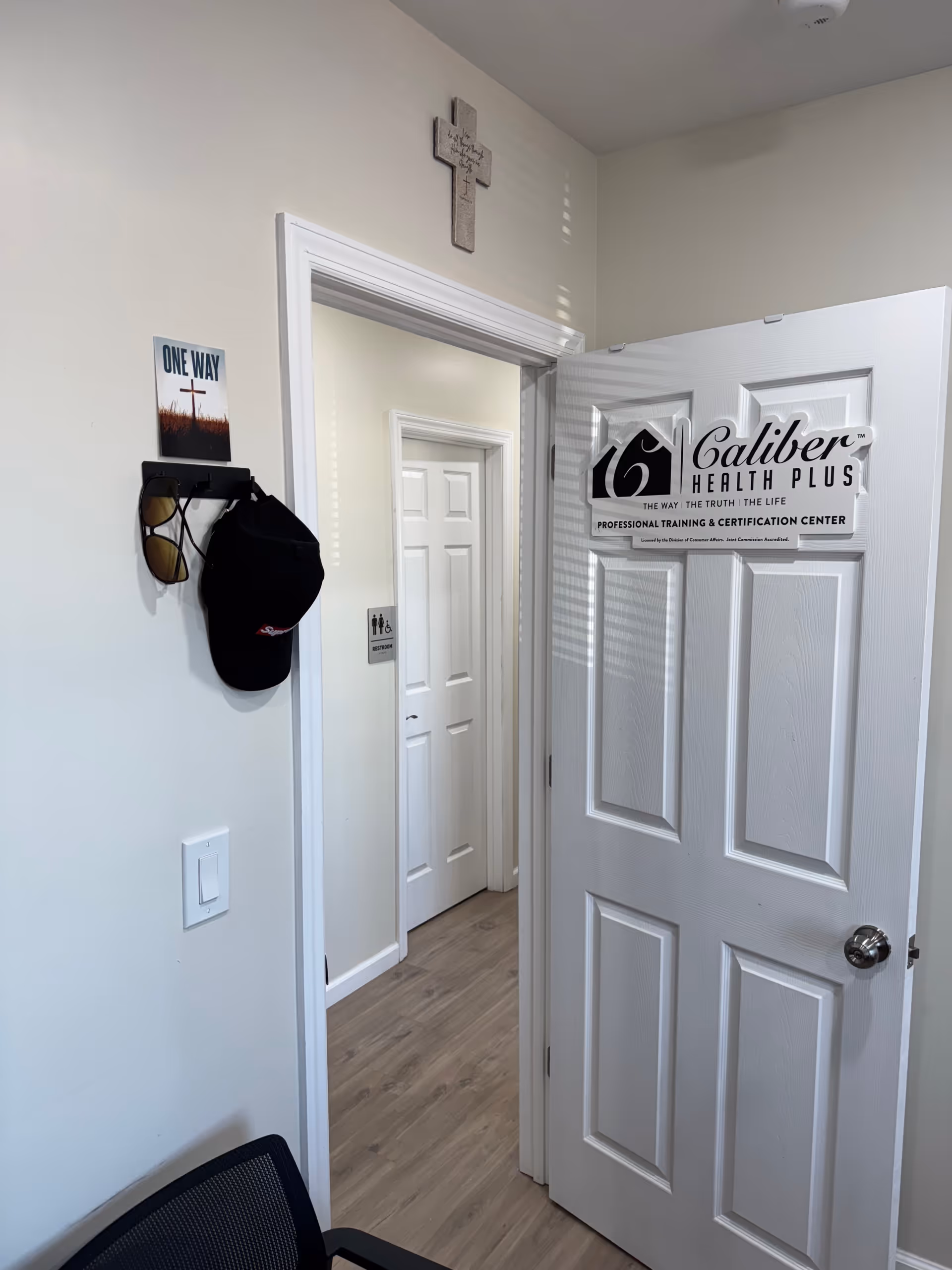 Interior hallway at Caliber Health Plus with doorway sign and wall cross.
