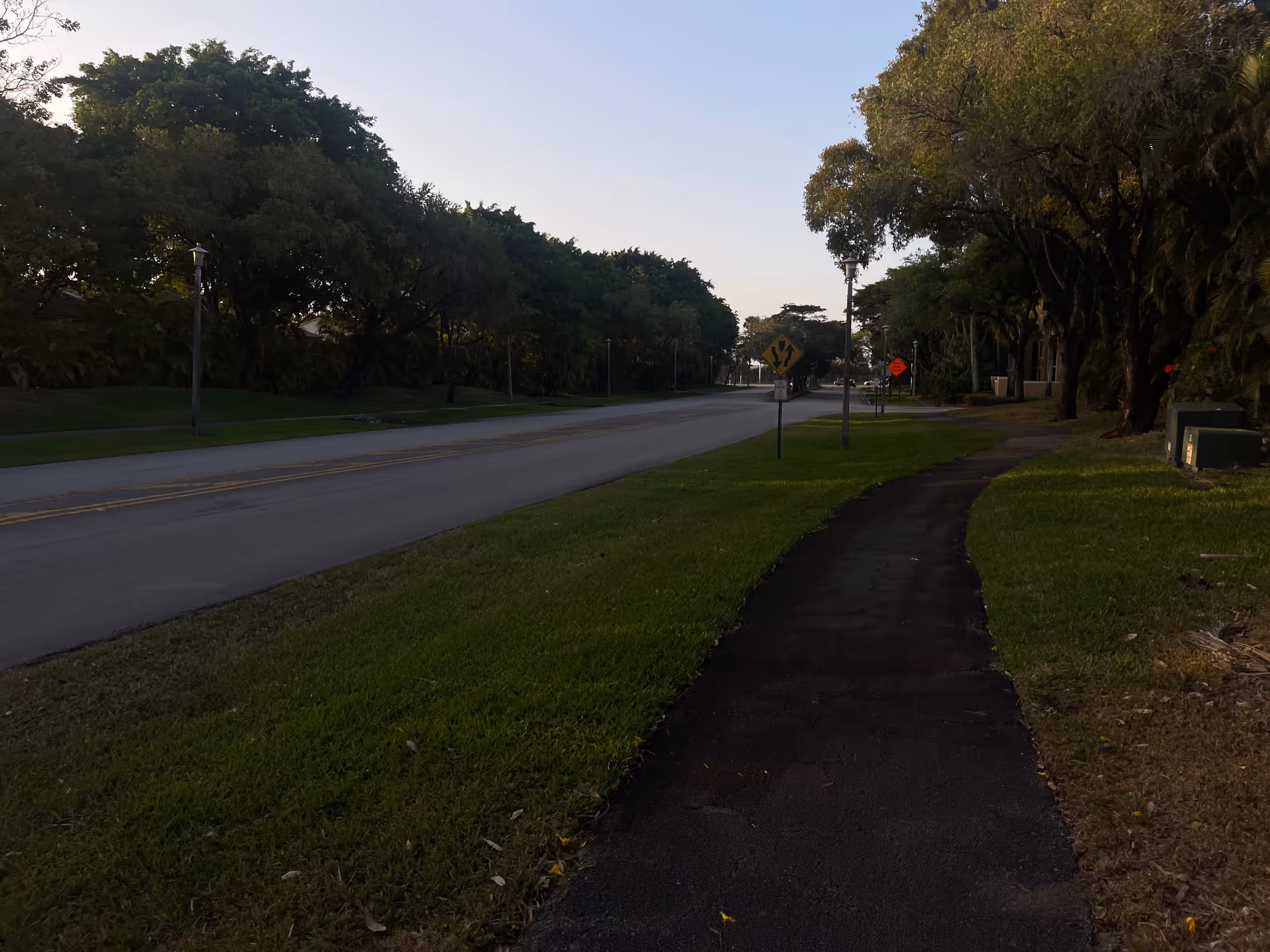 An exterior street view shows a sidewalk, grassy verge, and mature trees near a facility.