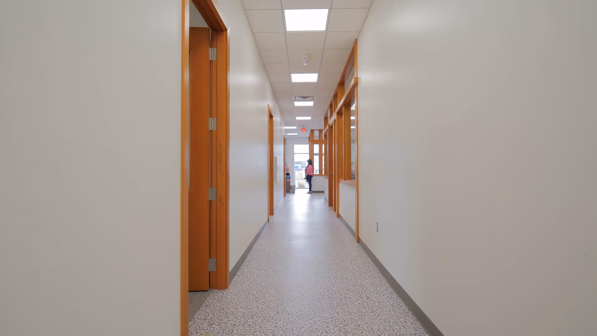 Long brightly lit hallway with wooden doors along white walls.
