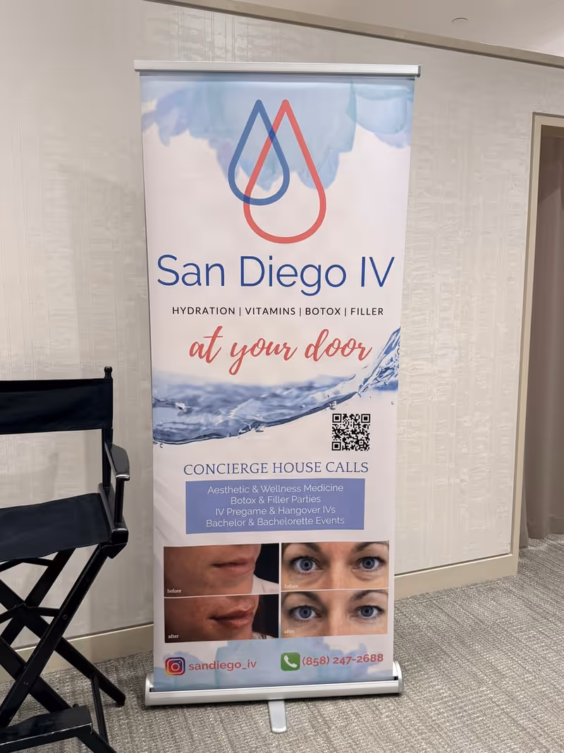 Indoor banner stand advertising San Diego IV mobile therapy with services, next to folding chair.