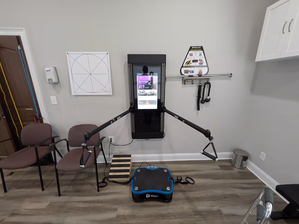 Rehabilitation station with adjustable arm supports, chairs, and a vibration platform in a small exercise room.