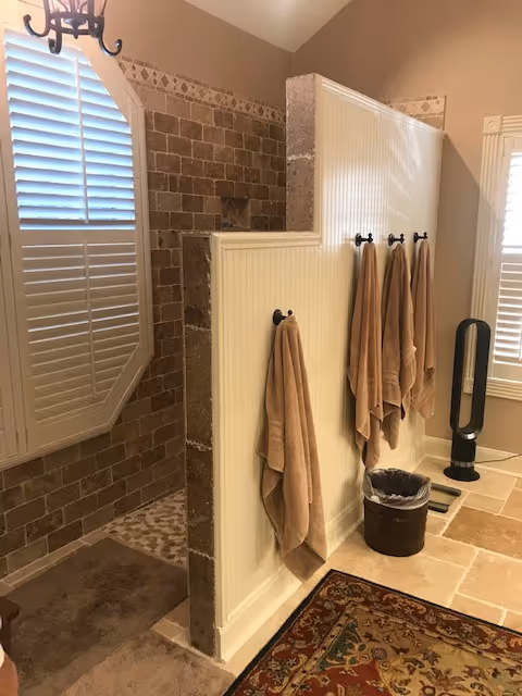 Bright bathroom with tiled shower, beadboard divider, towels, window blinds, and decorative rug.