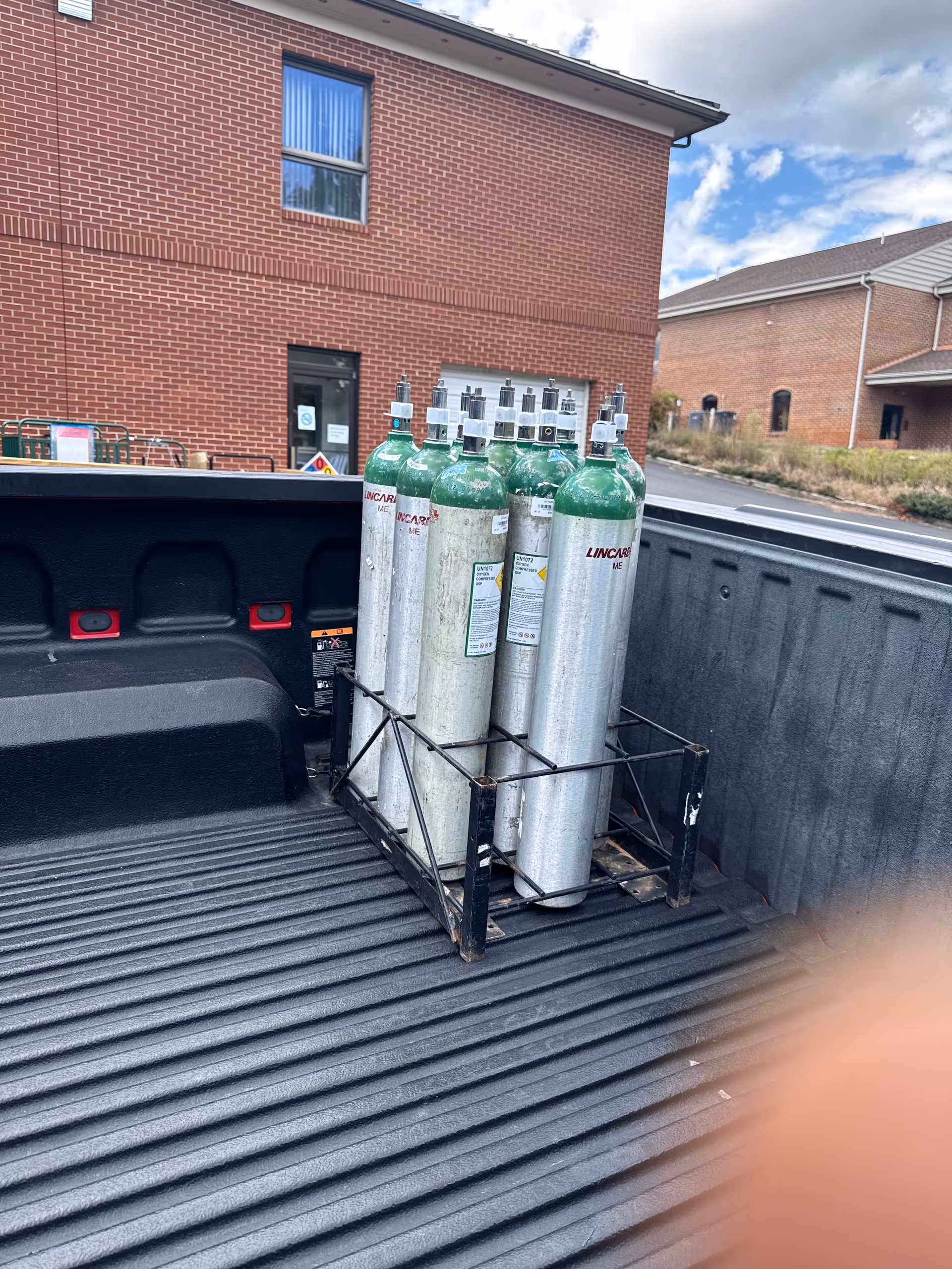 Back of a pickup truck loaded with Lincare oxygen tanks near a brick building.