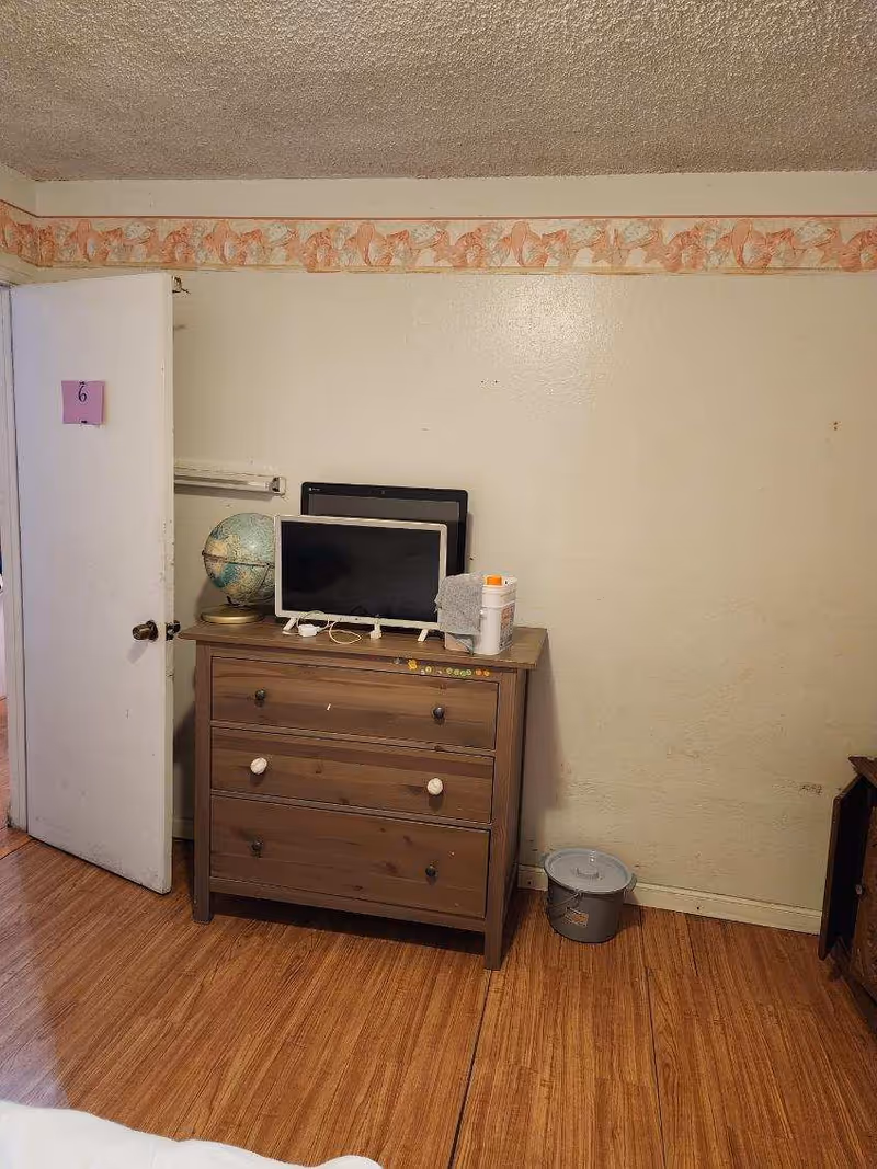A small bedroom with a wooden dresser, globe, monitor, and a door labeled 6.