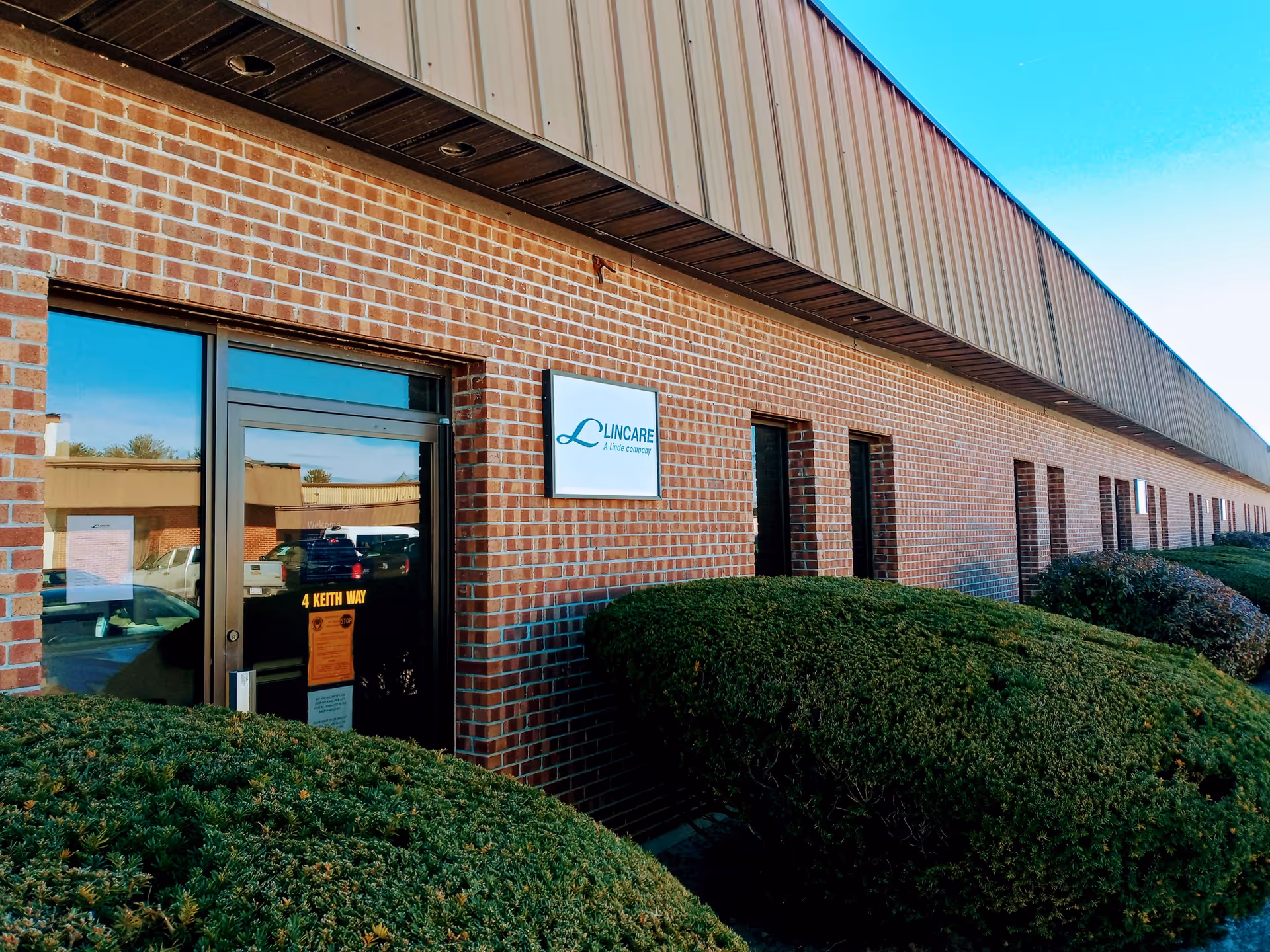 Exterior brick building with a Lincare sign, glass door, and trimmed shrubs.