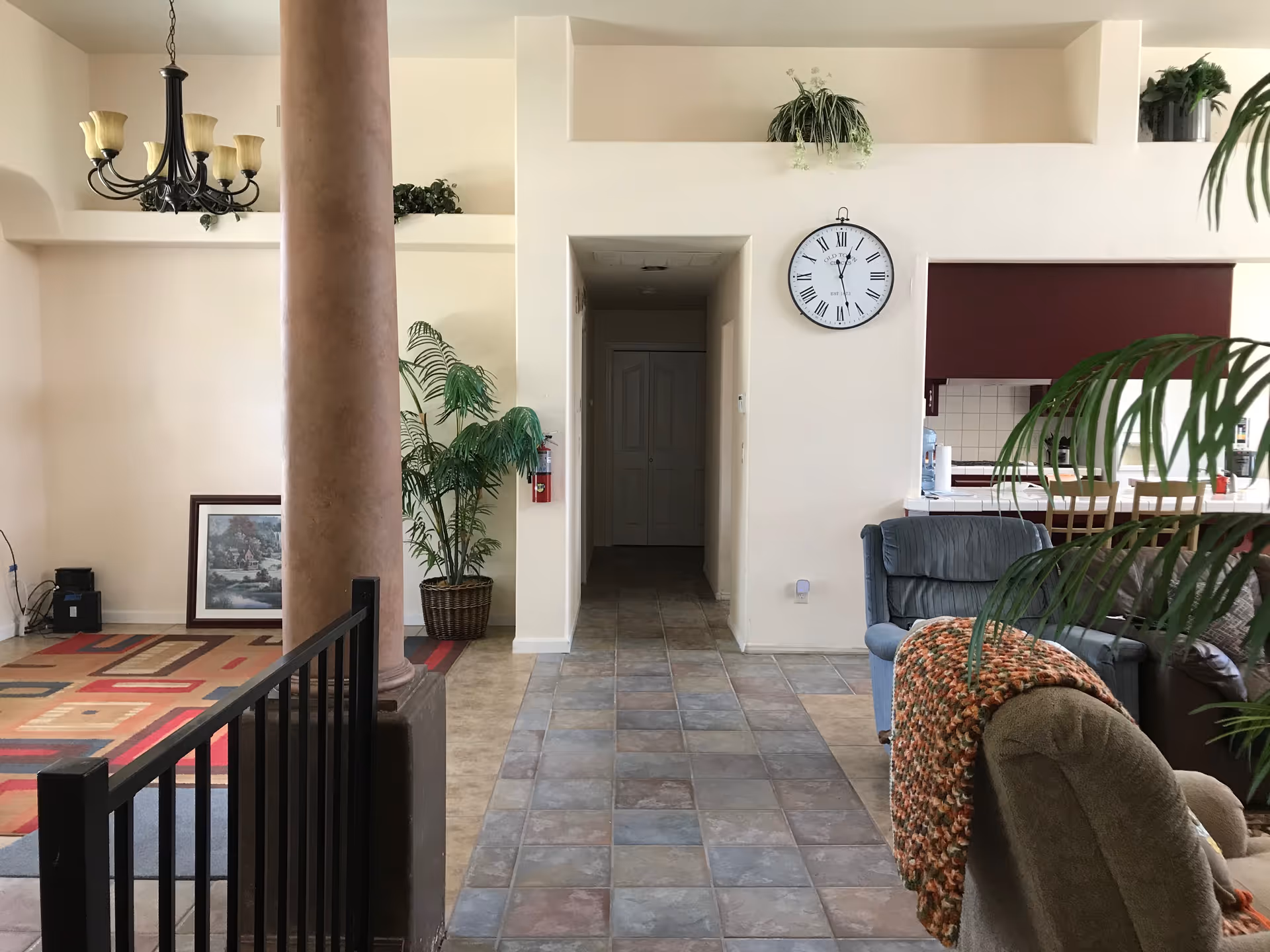 Interior common area with seating, plants, a clock, and a hallway in a senior living facility.