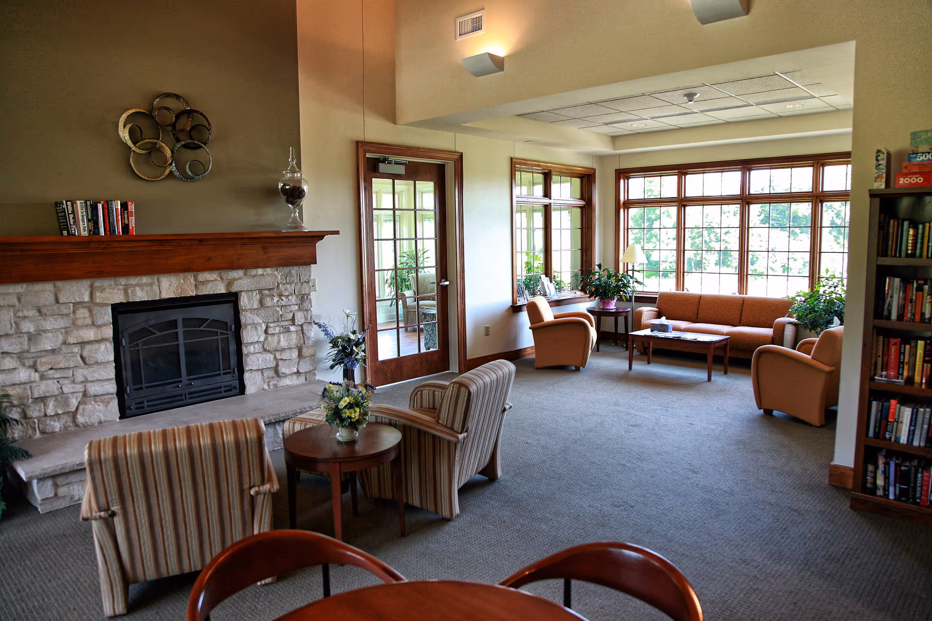 Cozy senior living lounge with a stone fireplace, seating area, and large windows.