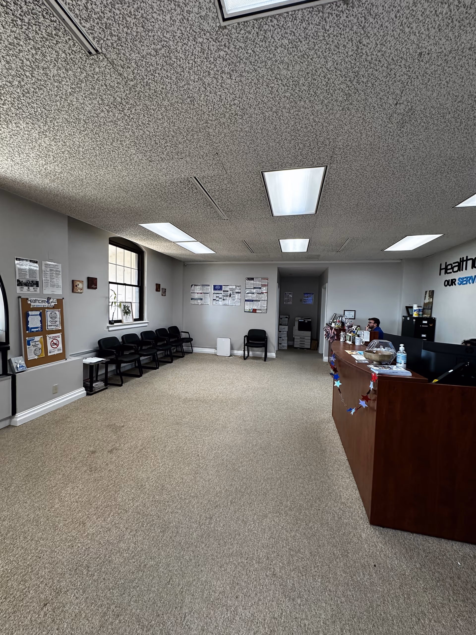 Reception area with a wooden counter, row of black chairs, and bulletin boards.