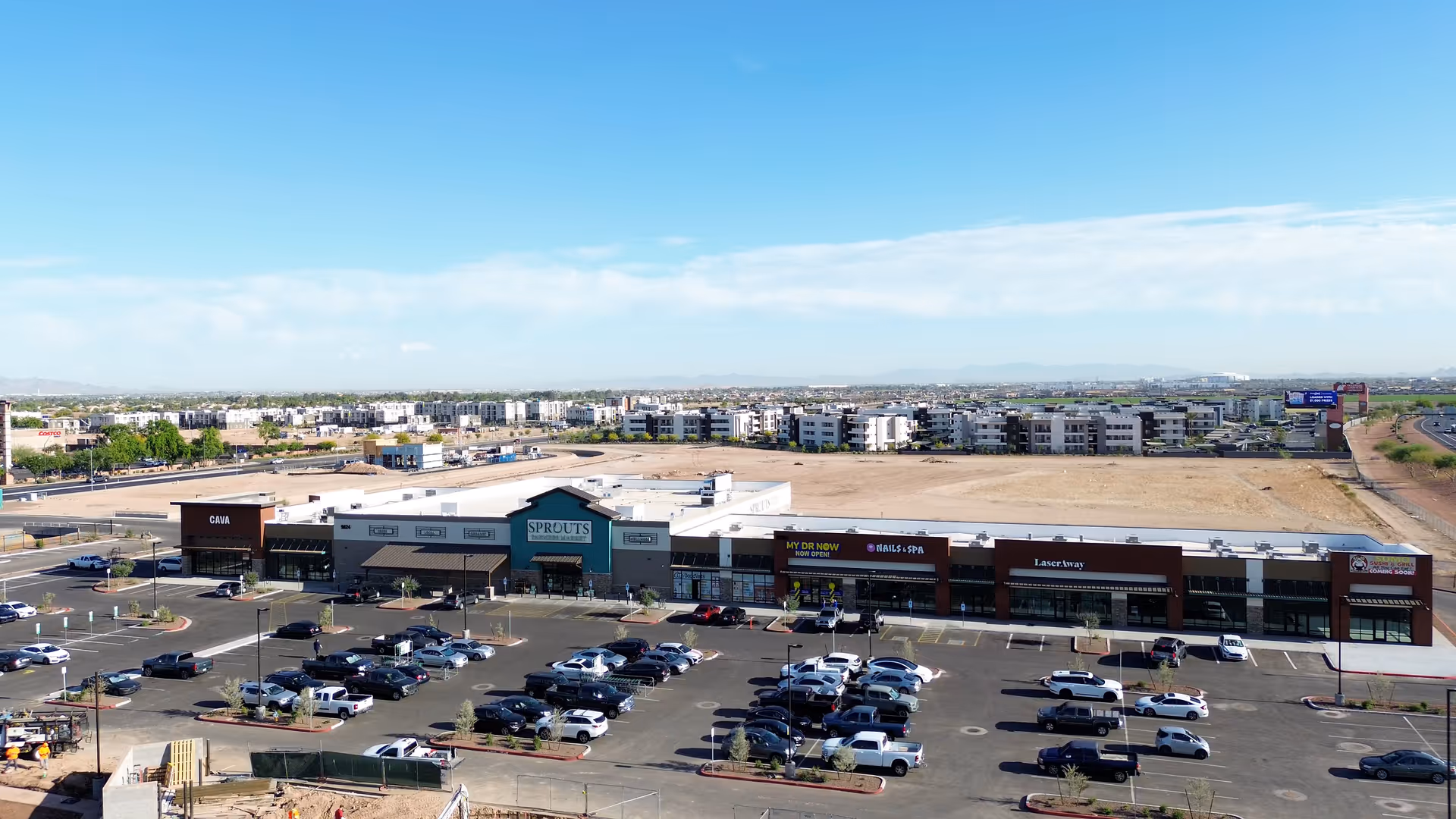 Wide view of a strip mall with Sprouts, parking lot, and distant residential buildings.