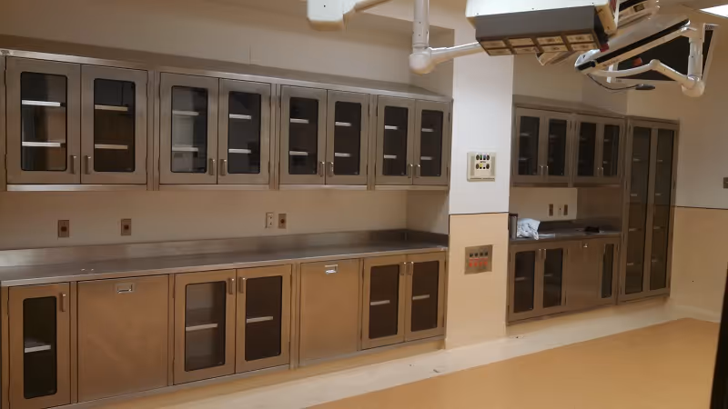 Sterile stainless steel cabinets and countertops beneath surgical lights in an operating room.