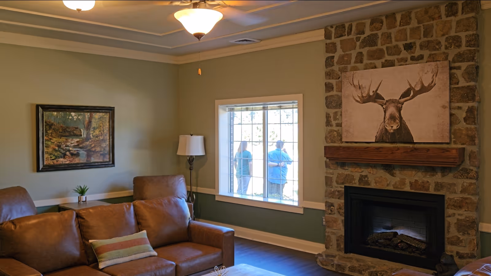 Cozy living room with leather sofa, stone fireplace, wall art, and a window showing people outside.