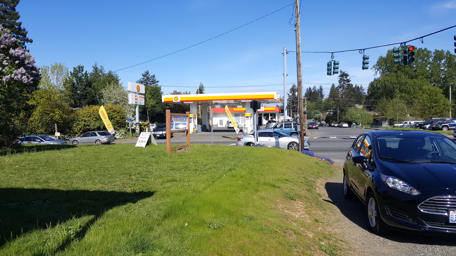 Street view with a grassy median, traffic lights, and a gas station in the distance.
