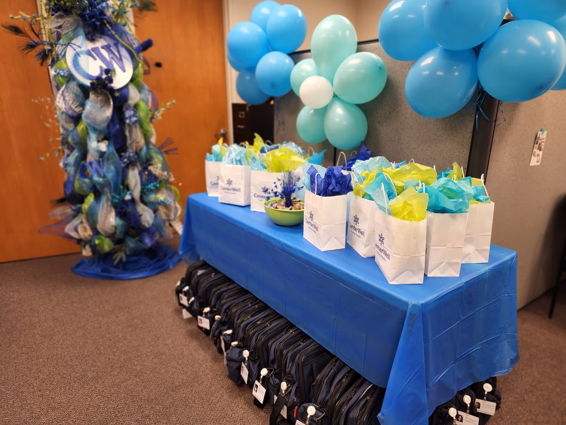 Table with gift bags and blue balloons for a CenterWell Home Health event in an office.