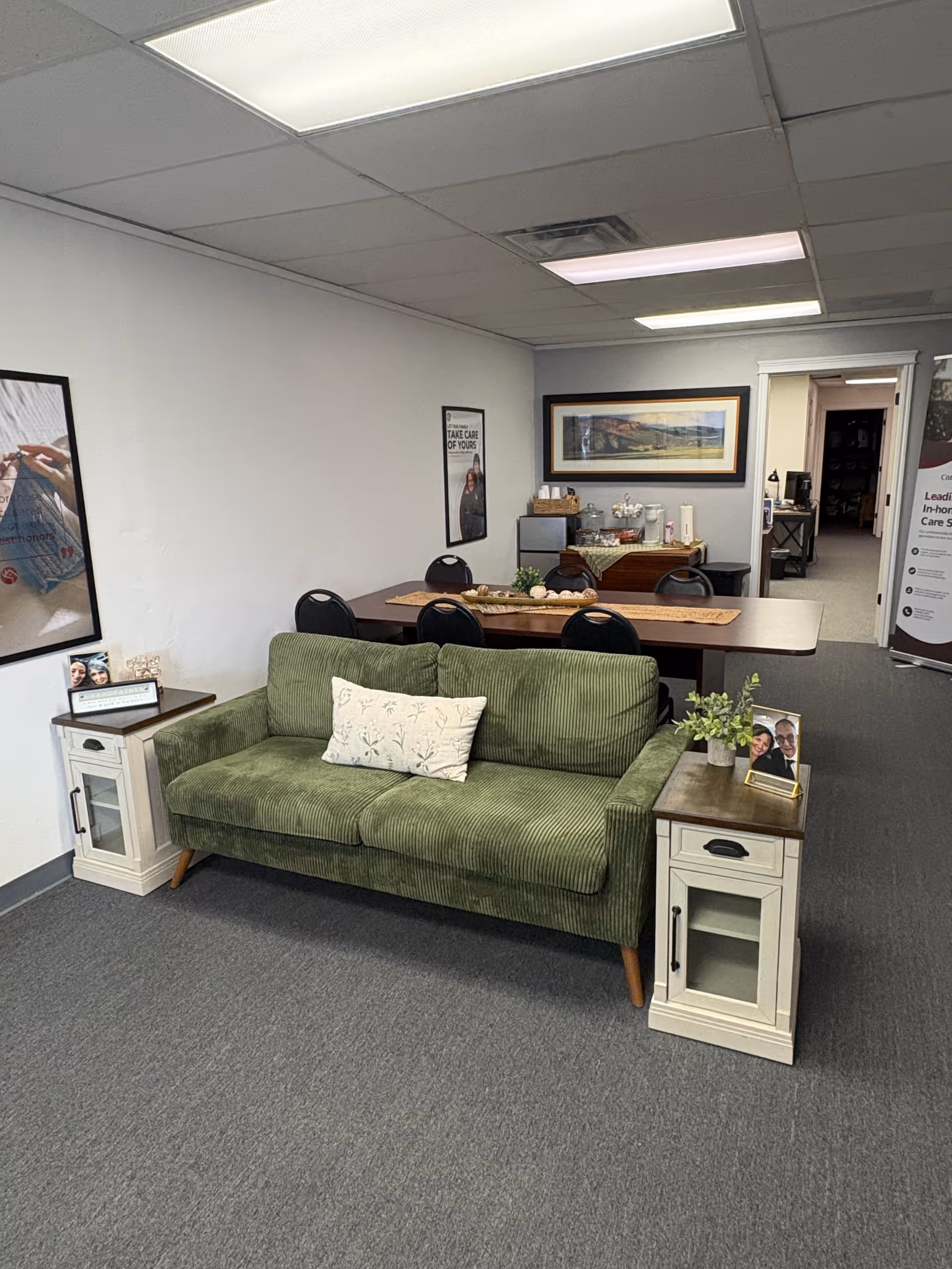 Green sofa with end tables in a quiet facility lounge, dining area visible in back.